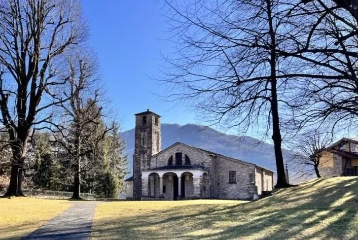 Vista di un lago con montagne verdi e un villaggio lungo la riva, vista dal punto di vista di una barca a motore con il cruscotto visibile.