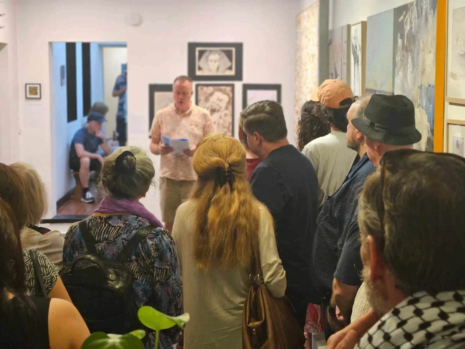 A group of people attending an art presentation in a gallery, listening to a person speaking .