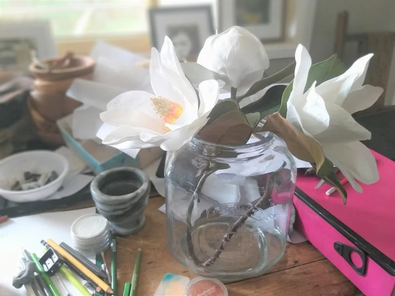 A timber table arrayed with art materials and white magnolia flowers.