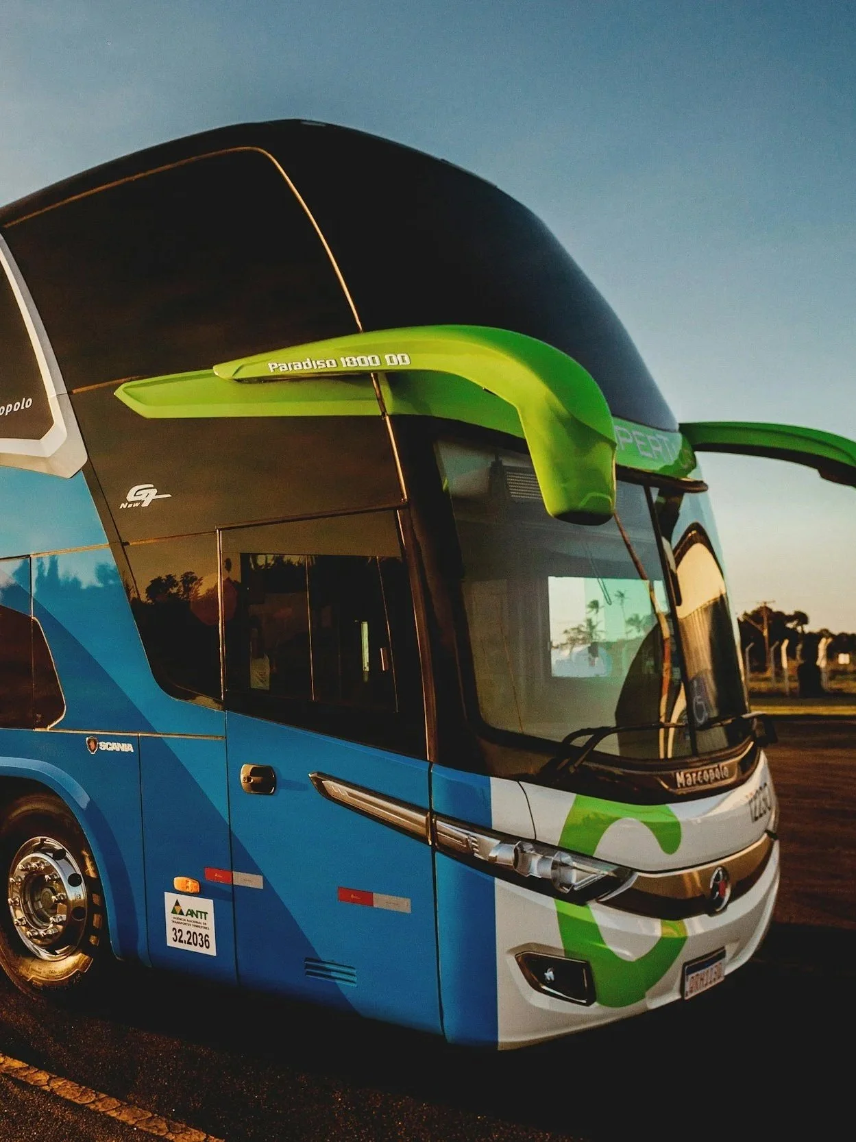 A double-decker bus painted in blue and white with green accents, parked outdoors during sunset.