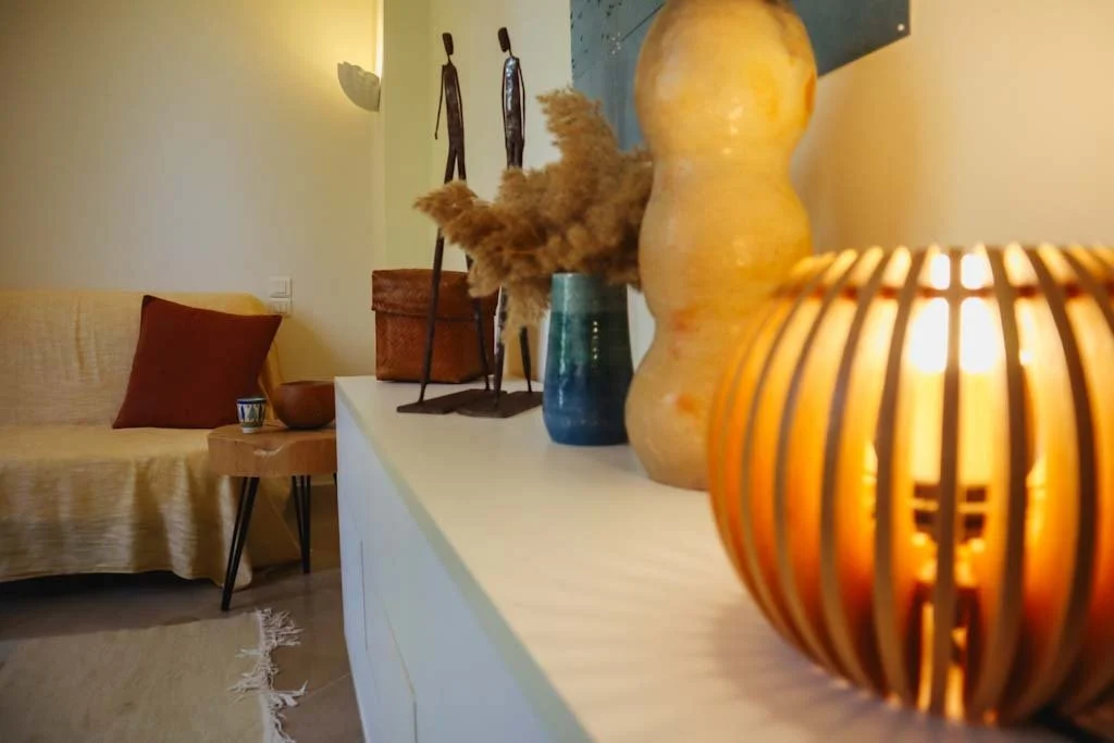 Une console avec des décorations telles que un vase, une lampe en rotin et deux figurines en bois dans un salon cosy.