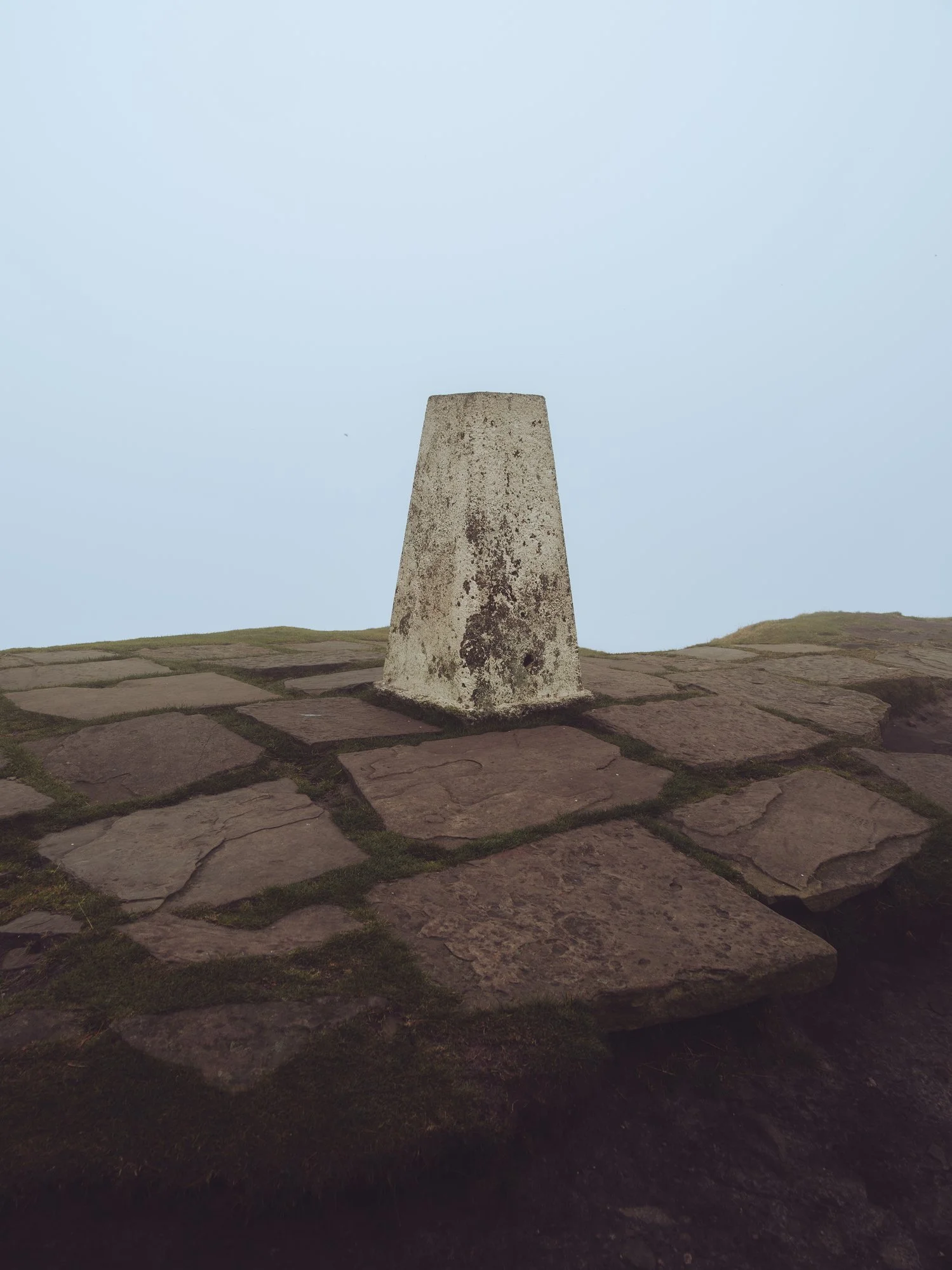 A stone trig point on a hilltop with a cloudy sky in the background.