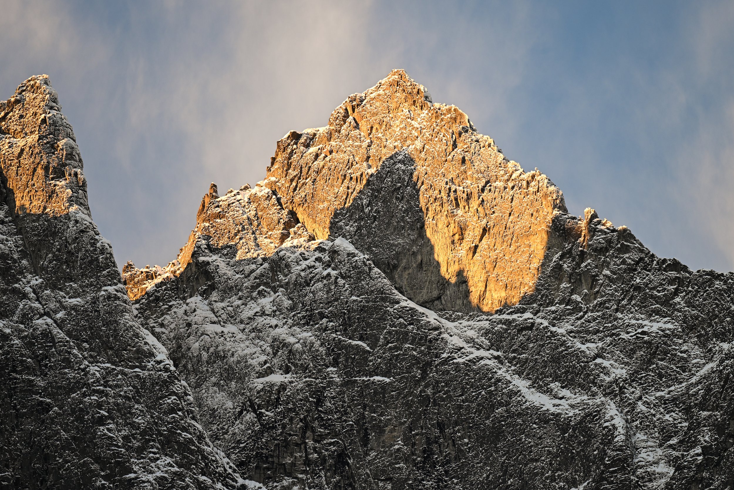 Snow-covered mountain peaks illuminated by sunlight with a cloudy sky background.