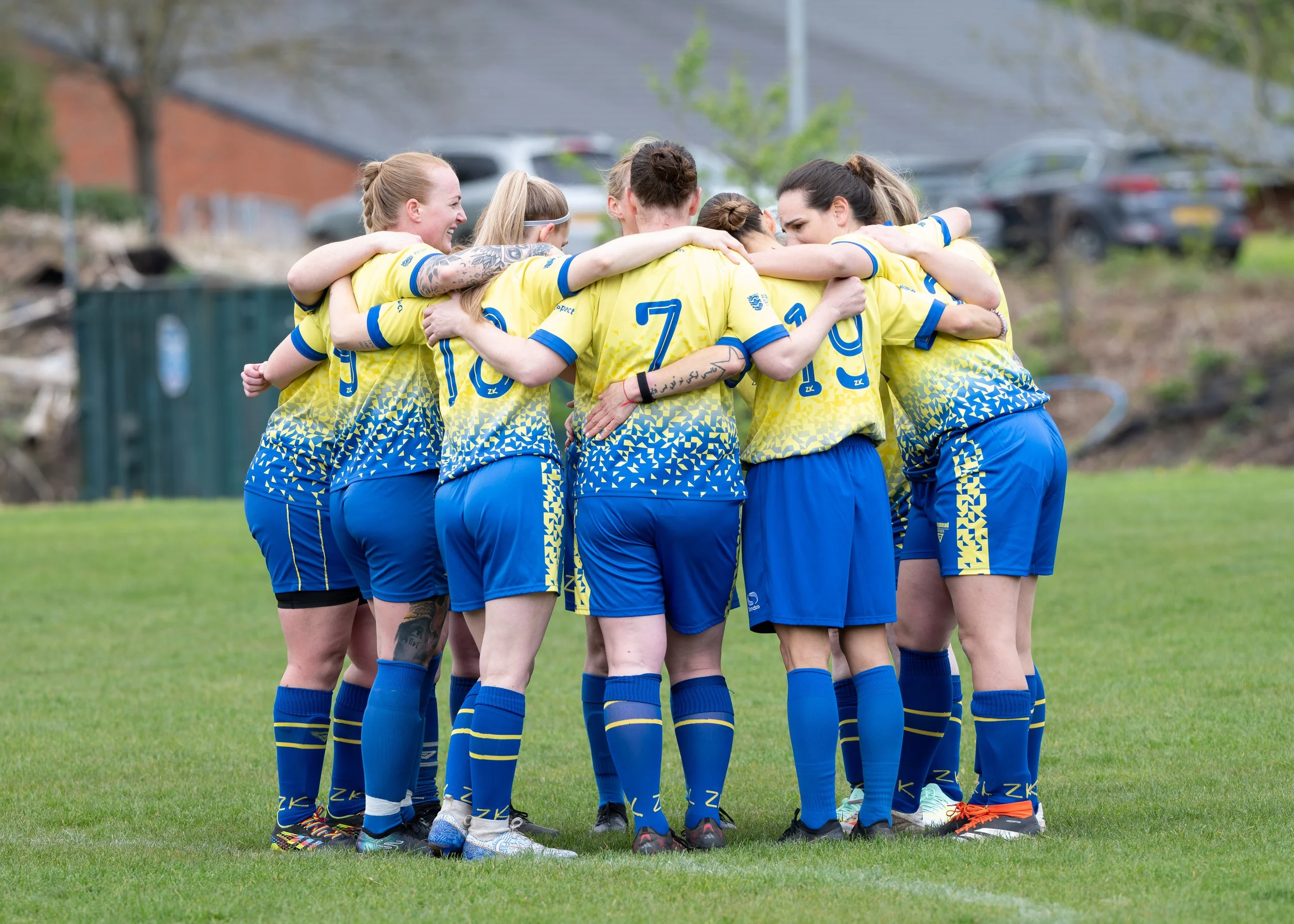 A group of female soccer players in yellow and blue uniforms huddle together on a soccer field.