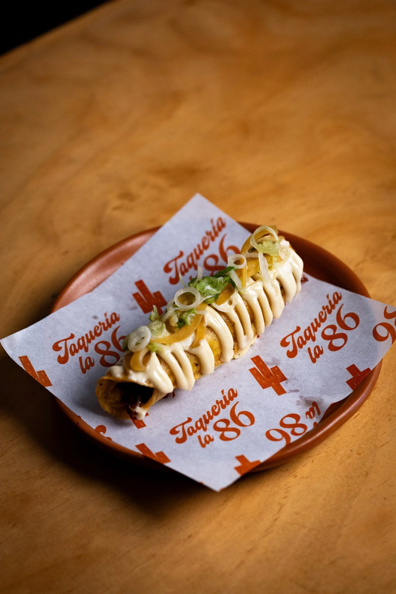 Taco de pollo dorado bañado con crema, queso, lechuga y cebolla en plato de barro