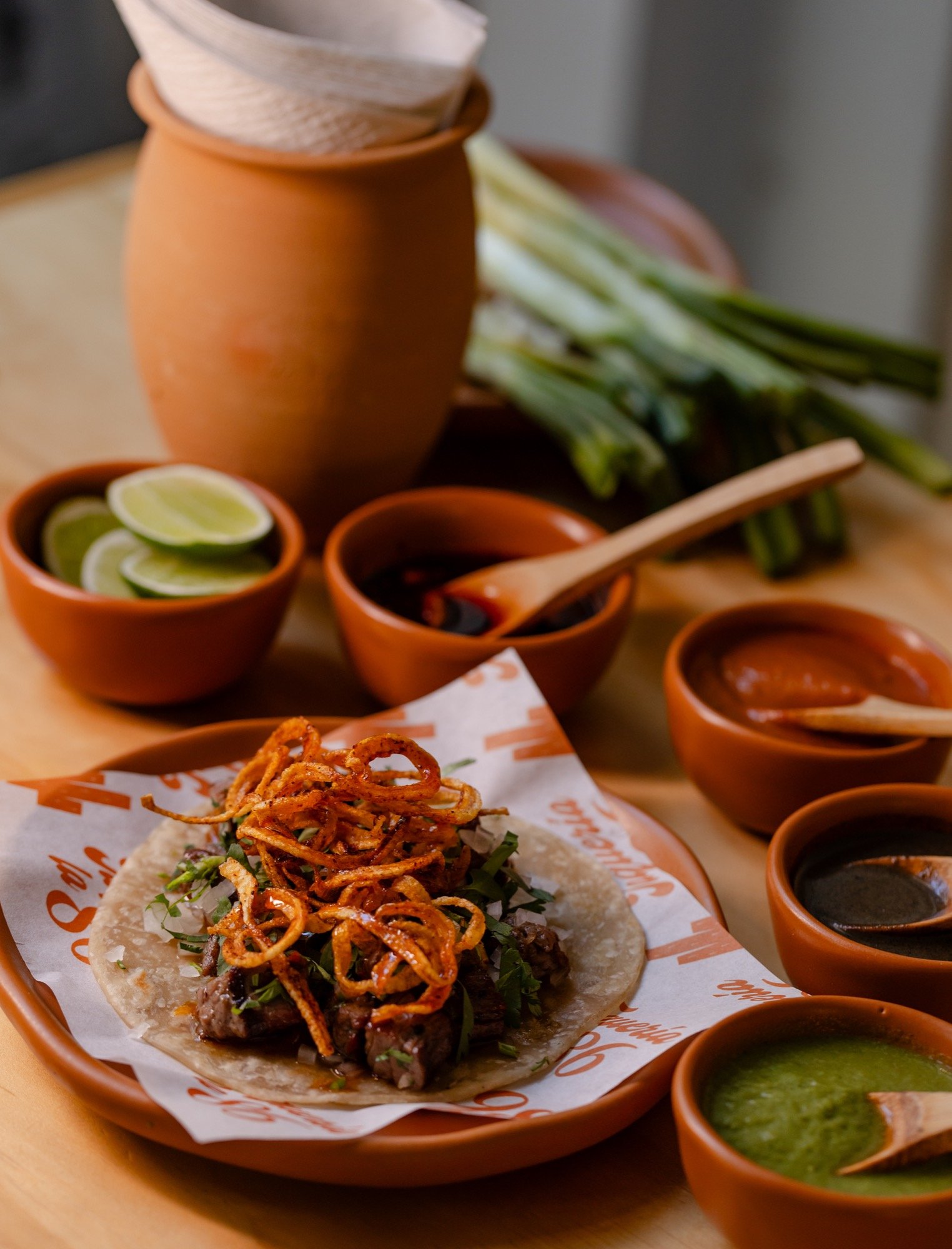 Taco de arrachera con cebolla frita crujiente y cilantro en plato de barro