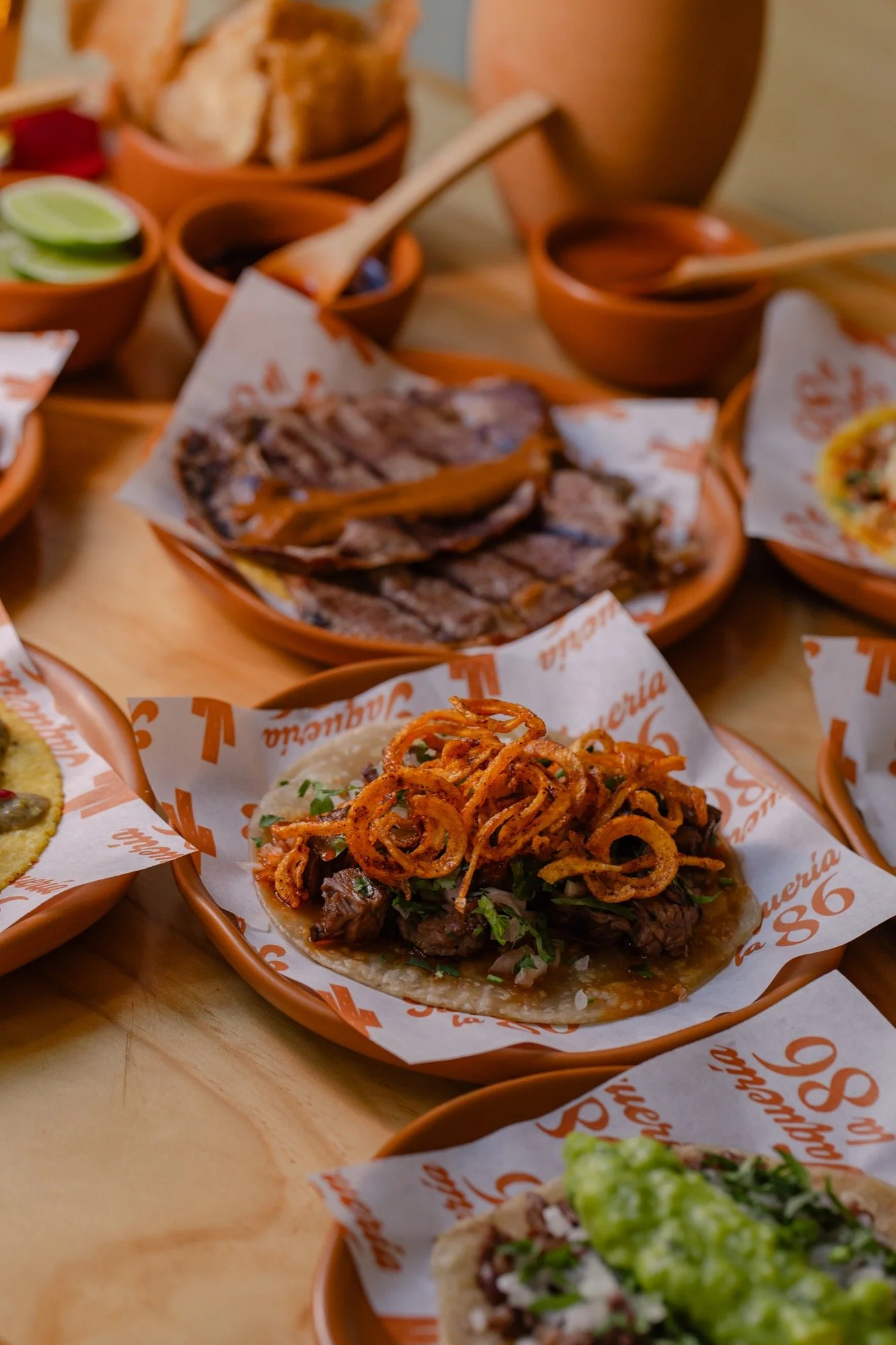 Mesa con varios tacos, cortes a la parrilla y salsas en cazuelas de barro