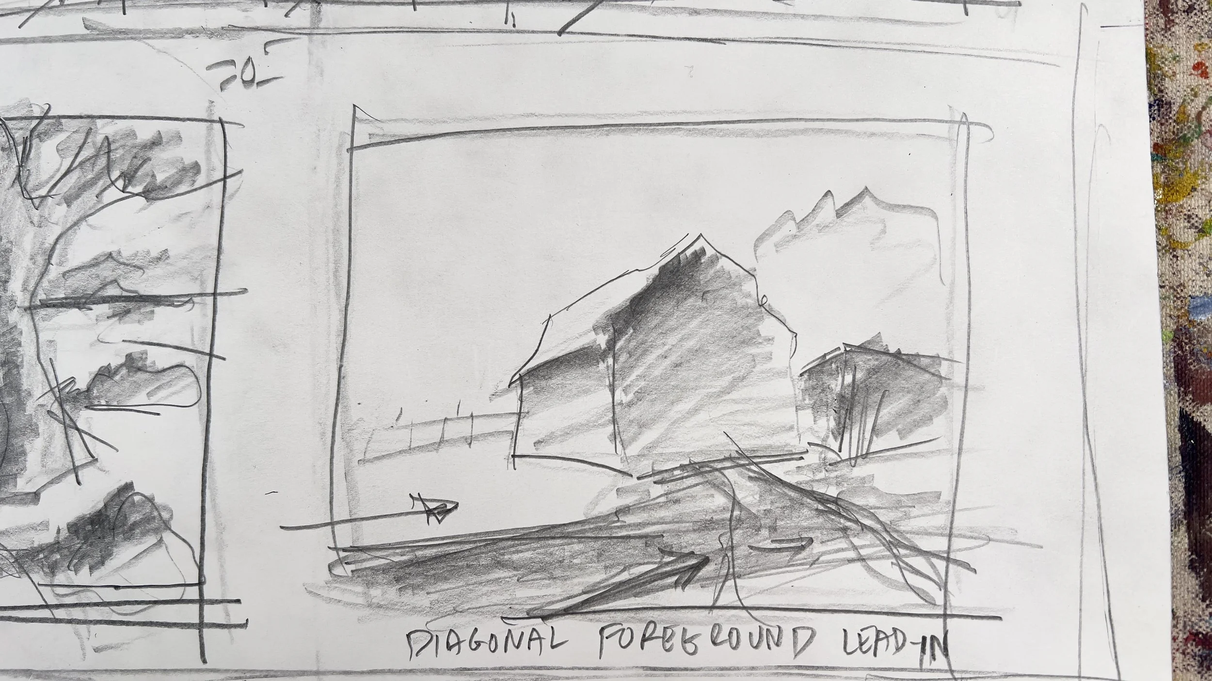 A black and white sketch on paper showing a landscape with mountains, a small building, and trees. The sketch has handwritten notes at the bottom reading 'Diagonally Foreground Lead In'.