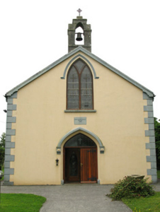 A small church with a beige exterior and gray stone accents, featuring a wooden door, a large arched window above, and a bell tower on top.
