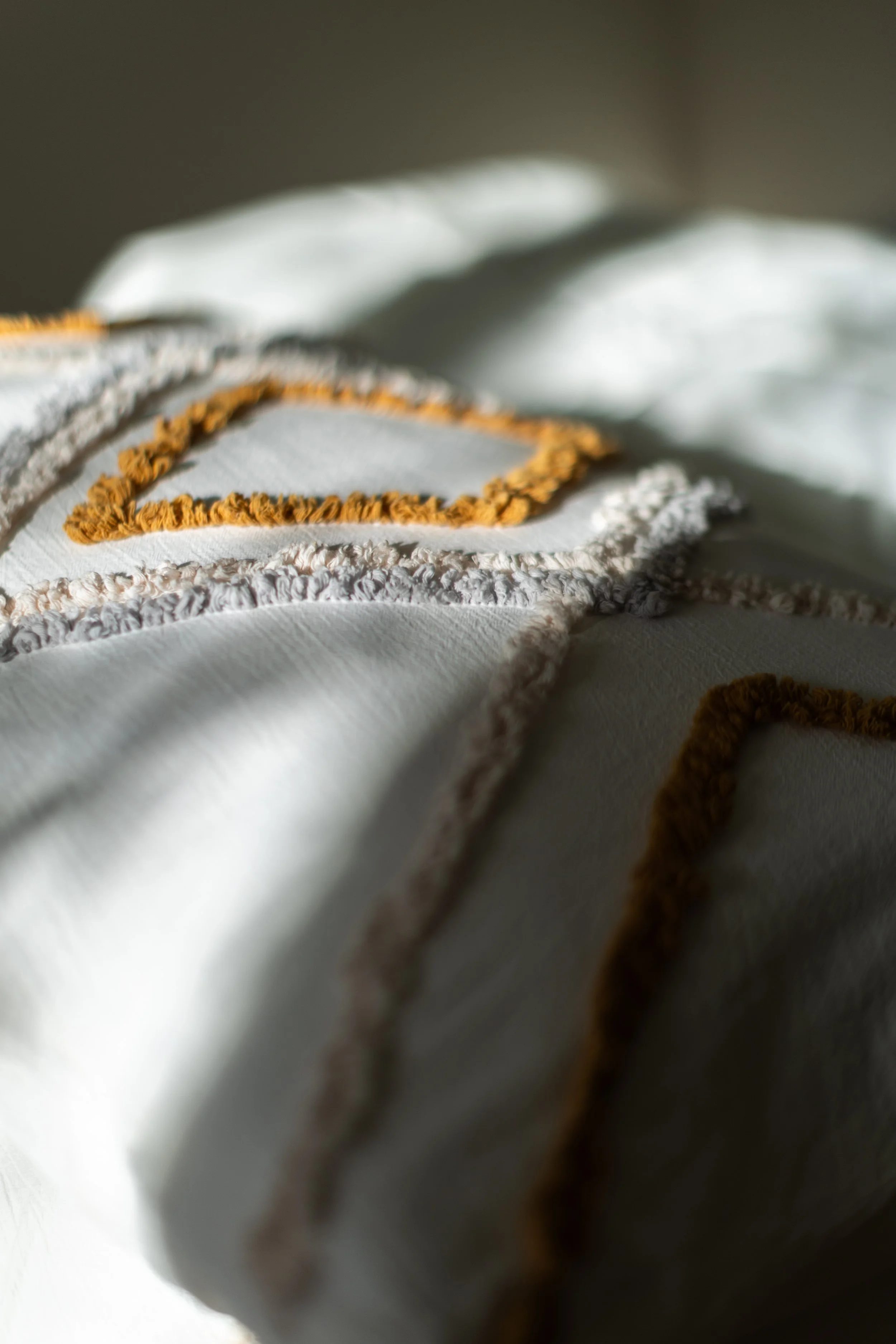 Détail d'un tissu blanc avec des broderies ou appliqués en coton de couleur jaune et beige.
