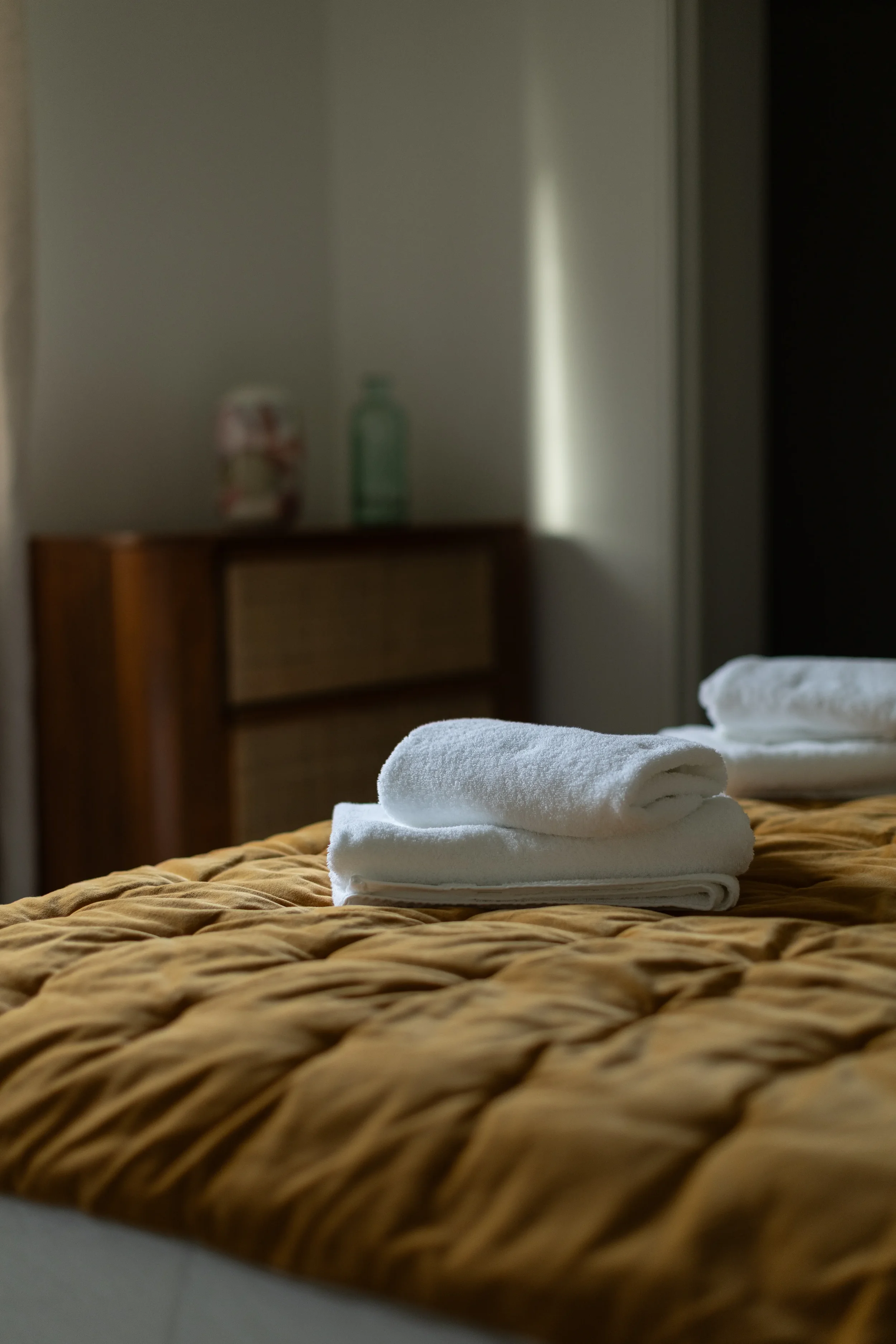 Des serviettes blanches pliées sur une couverture beige en texture zébrée dans une chambre, avec un meuble en bois flou en arrière-plan.