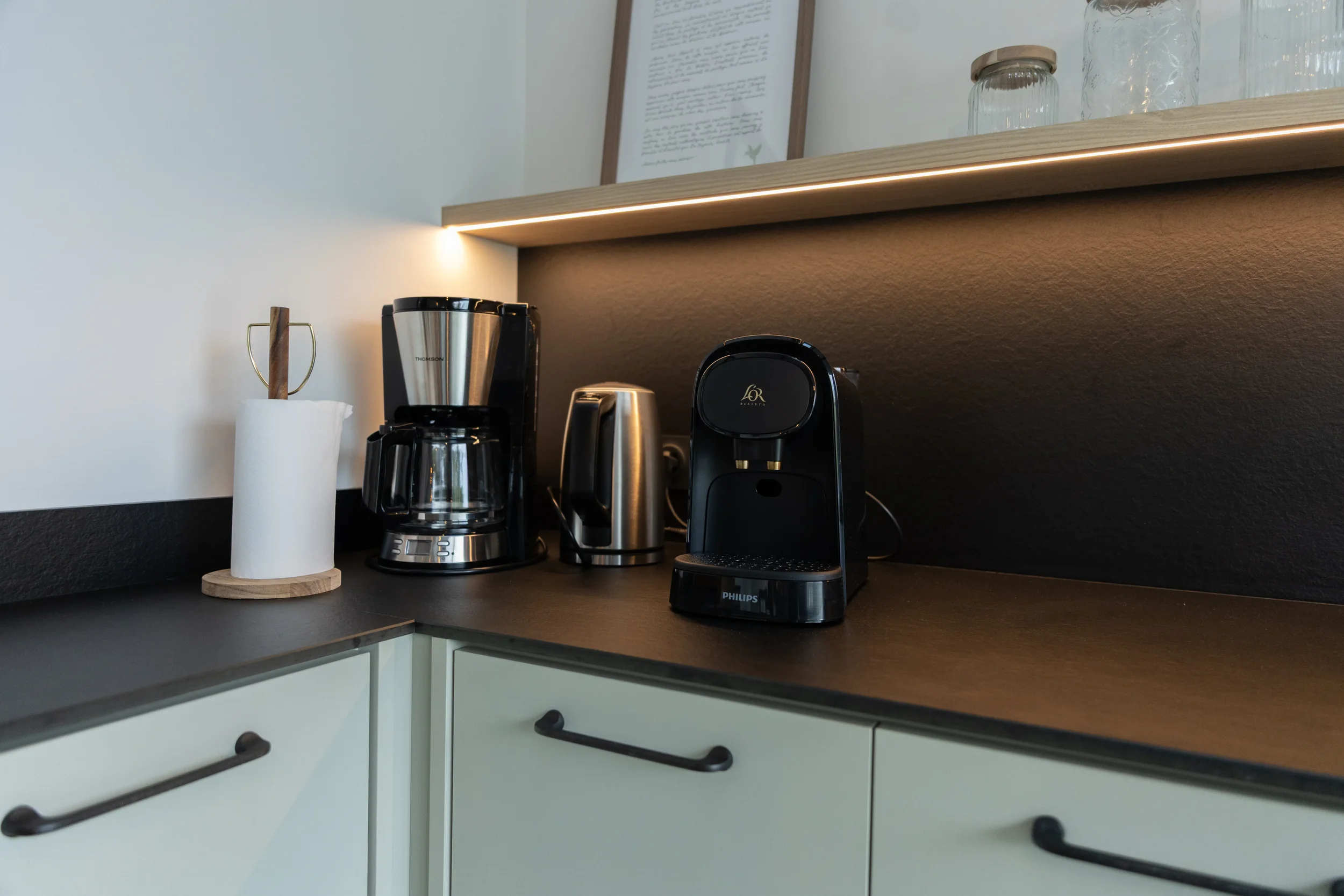 Coin café avec une cafetière, une bouilloire électrique, un percolateur et un support à essuie-tout sur un plan de travail en bois, dans une cuisine moderne.