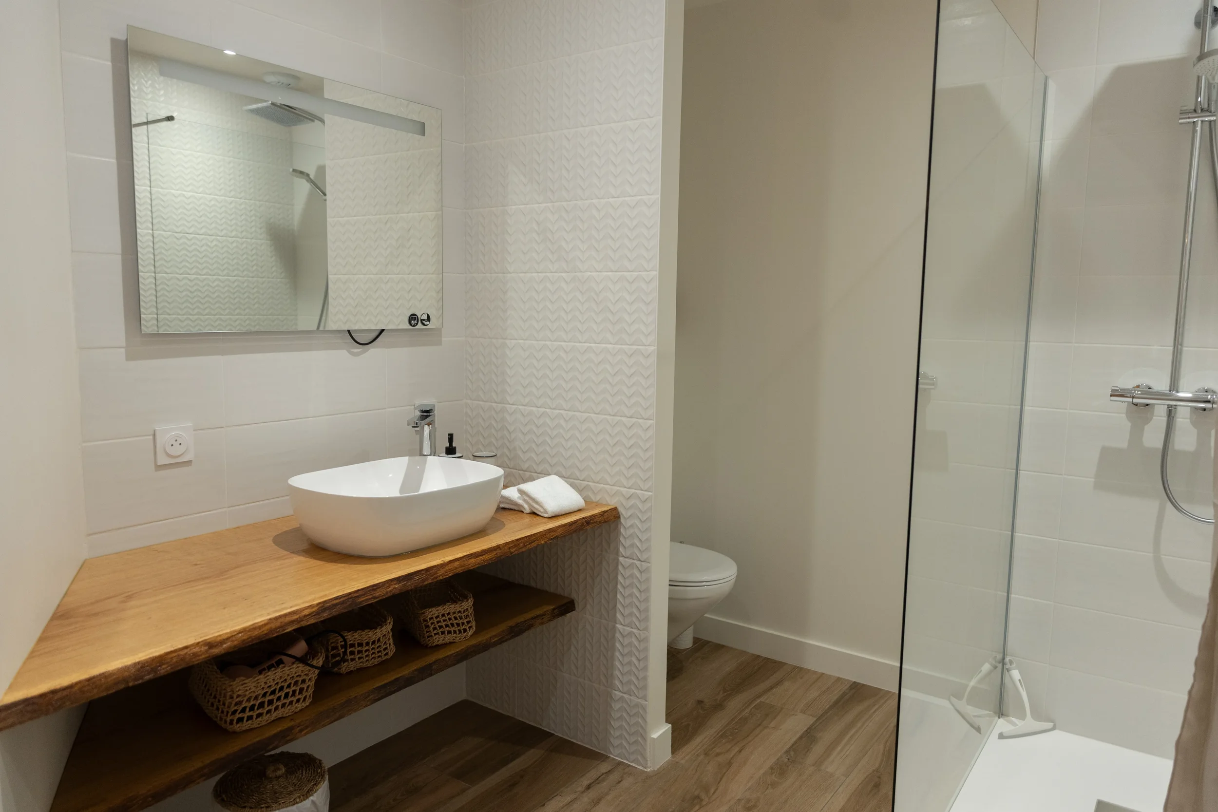 Salle de bain moderne avec lavabo sur planche en bois, miroir, douche à l'italienne et toilettes.