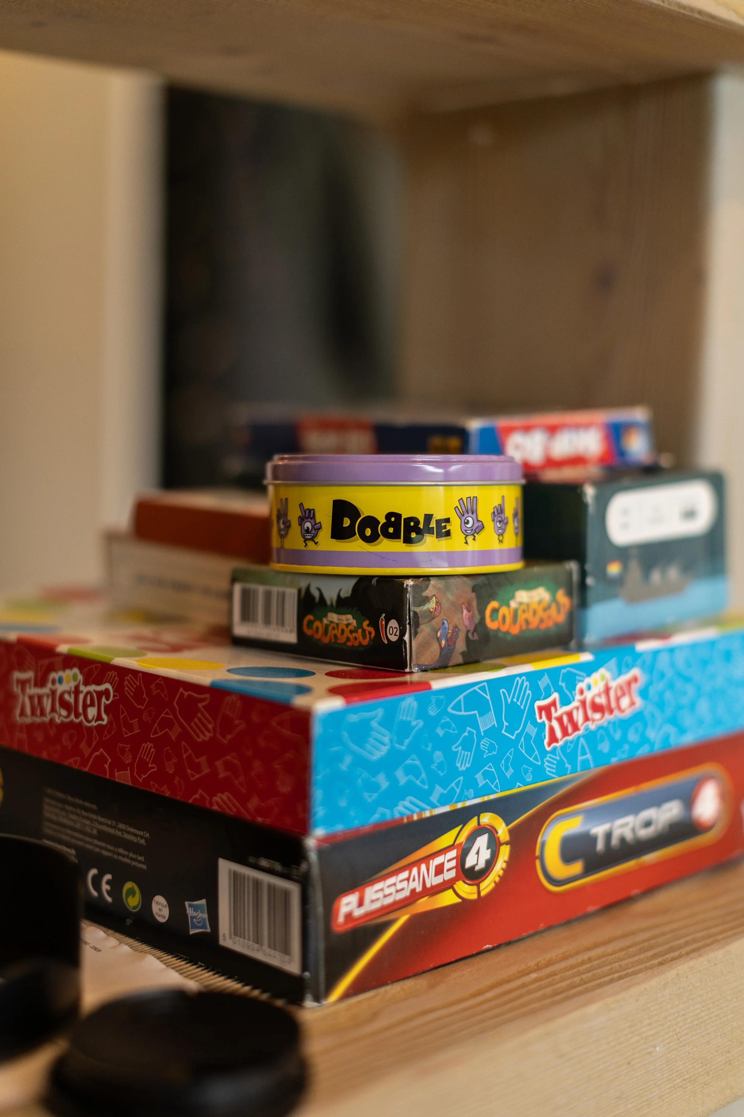 Une pile de plusieurs boîtes de jeux de société et de cartes avec un petit objet noir au premier plan.