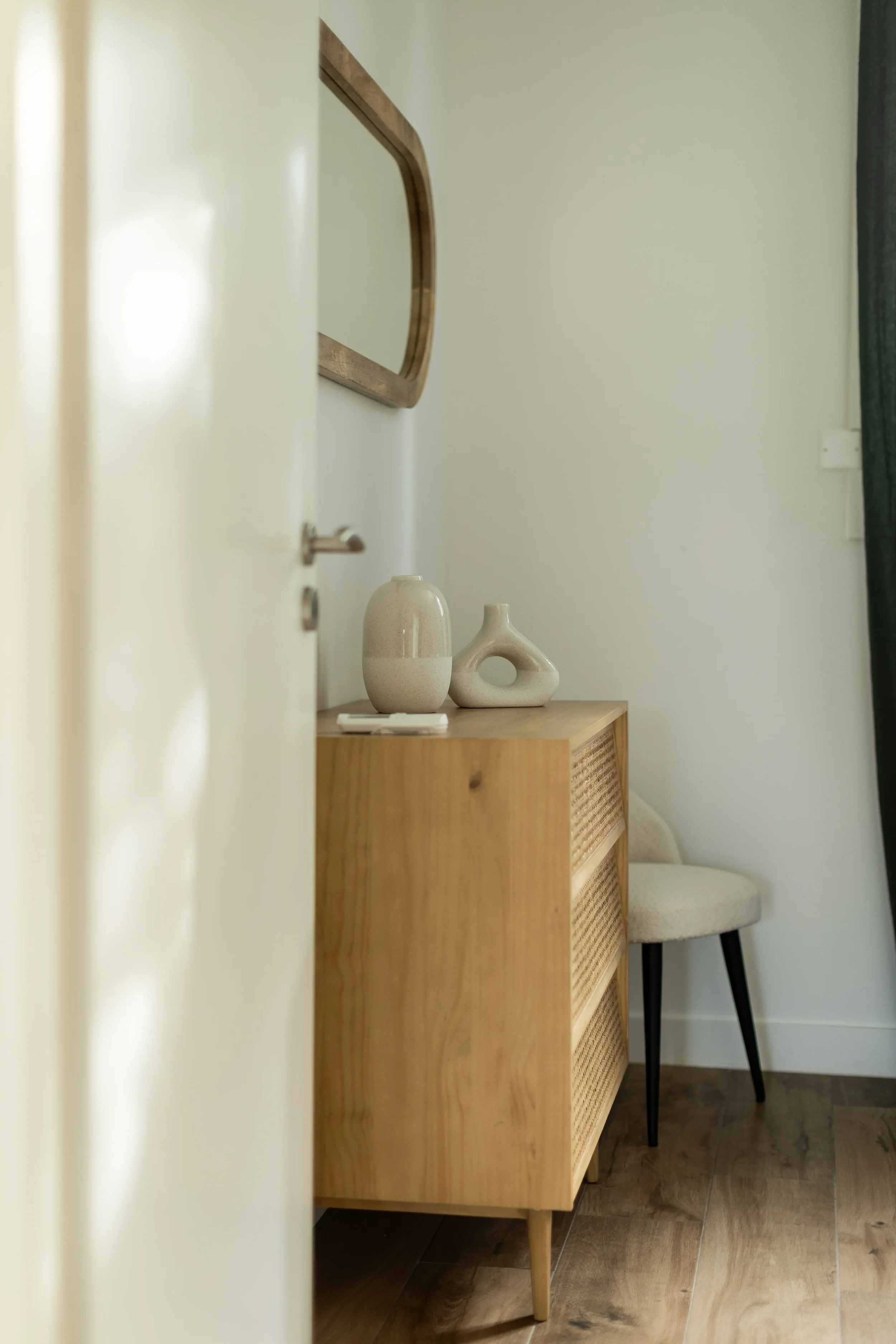 Une pièce intérieure avec un meuble en bois clair, une chaise blanche et des décorations en céramique sur le meuble, dans un style minimaliste.