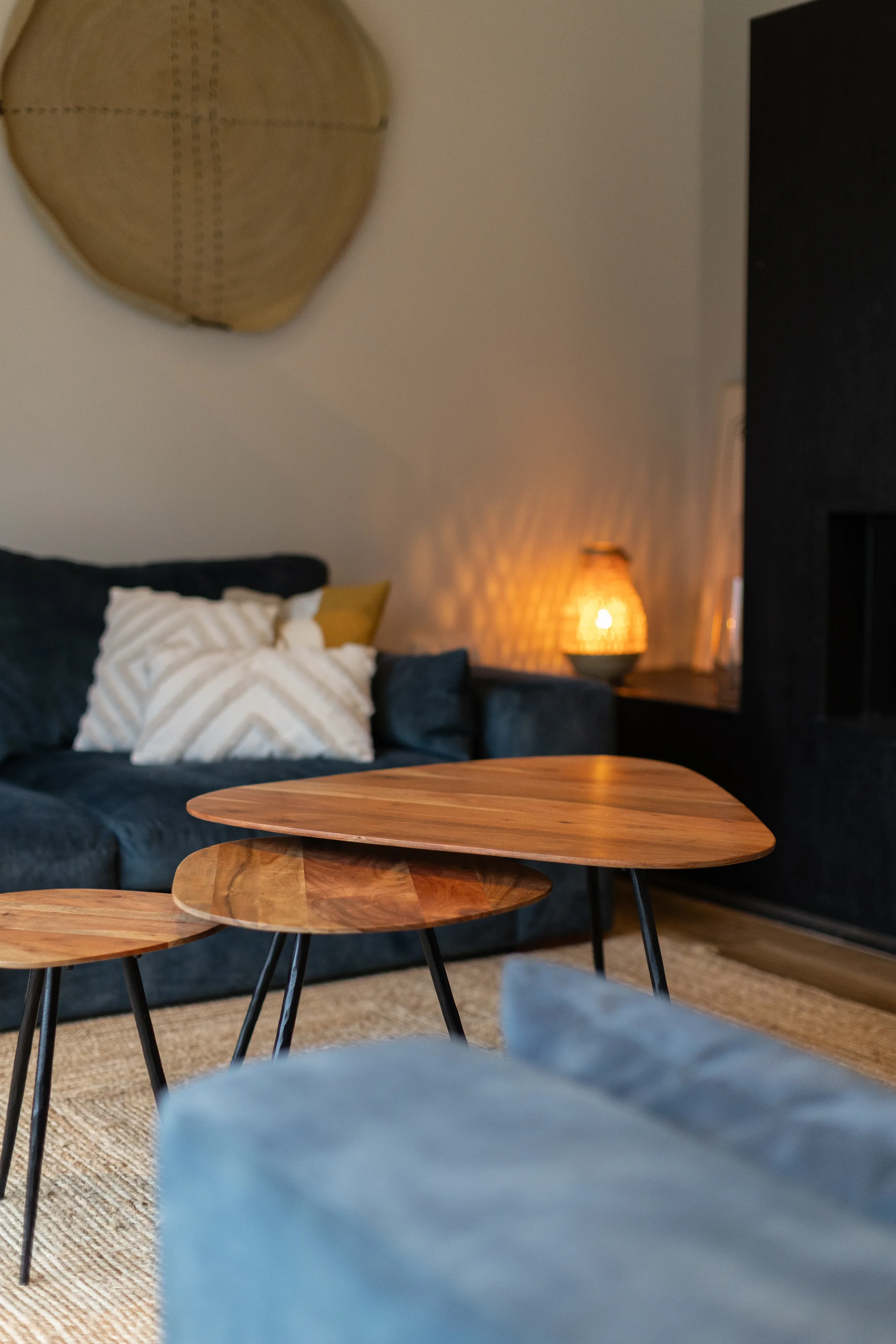 Intérieur d'un salon avec un canapé bleu, des coussins avec motifs géométriques, une table en bois, un tapis en fibres naturelles, une lampe à l'orientale avec une lumière douce, un mur blanc avec une décoration en osier.