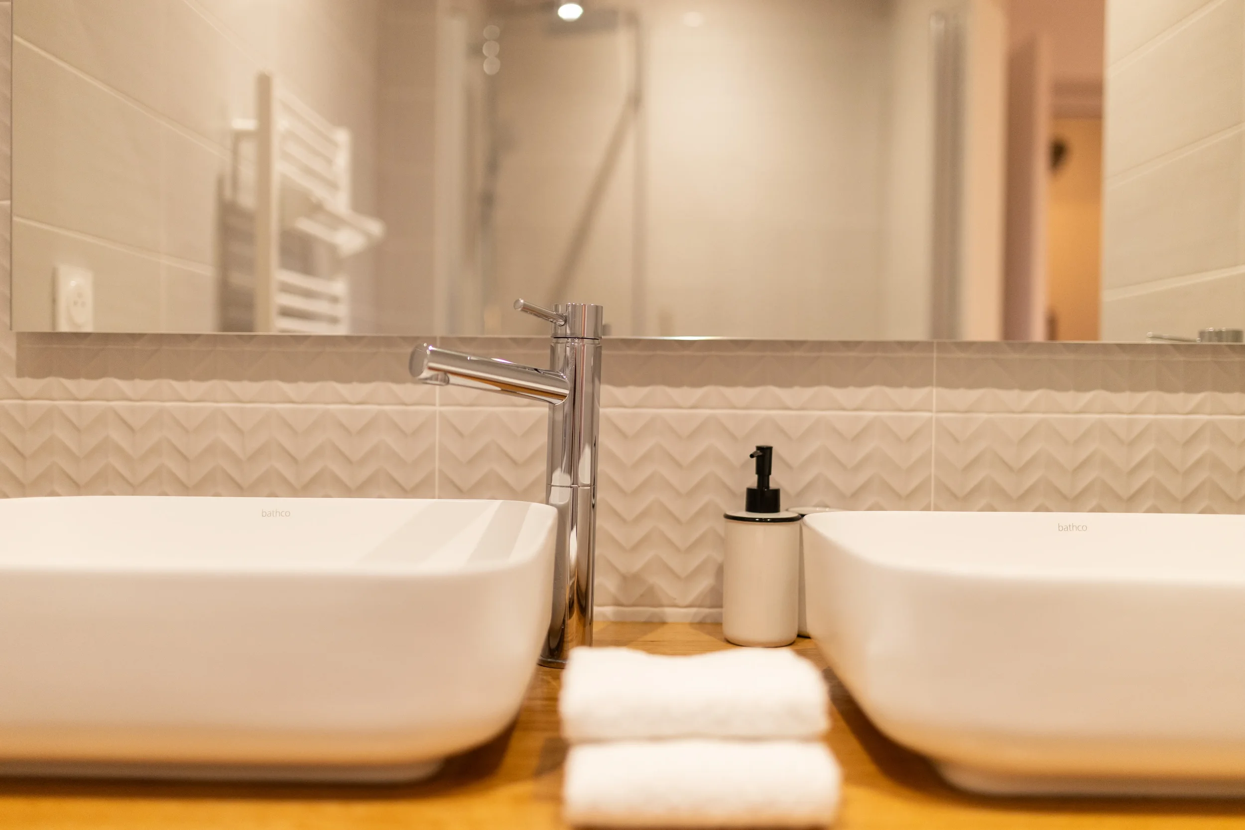 Vue rapprochée de deux lavabos blancs avec un miroir, un distributeur de savon et des serviettes sur un comptoir en bois dans une salle de bain