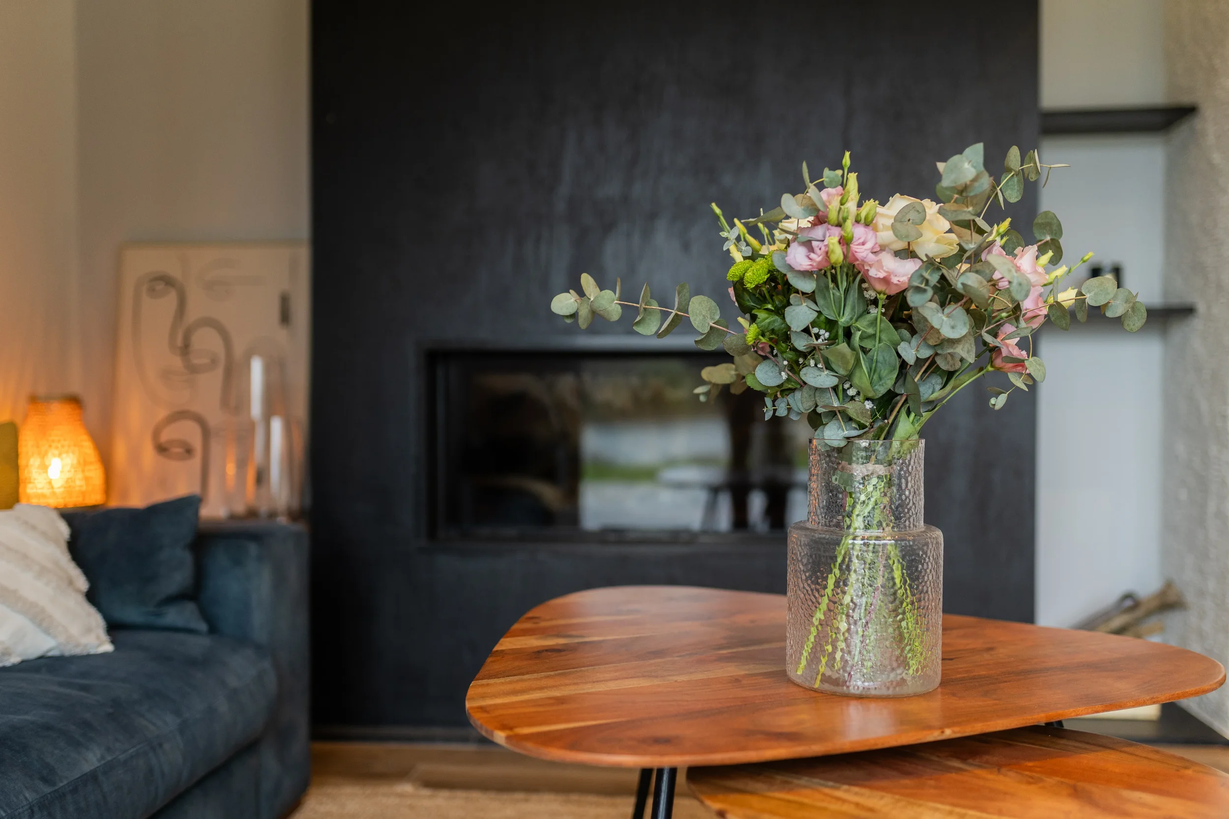 Vase en verre transparent avec bouquet de fleurs roses et vertes sur une table en bois dans un salon moderne.