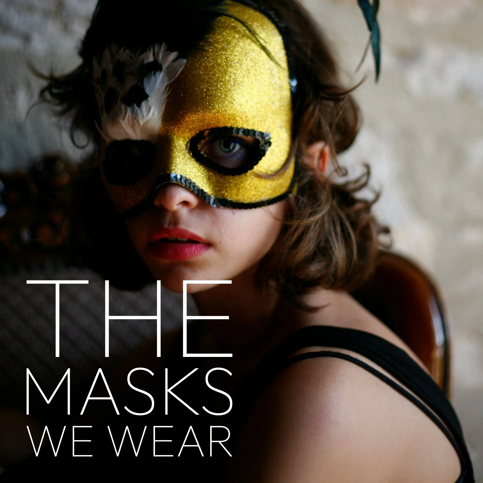 Close-up of a person wearing a yellow and black mask, with feathers, curlers, and curly hair visible, overlaid with white text reading 'THE MASKS WE WEAR'.