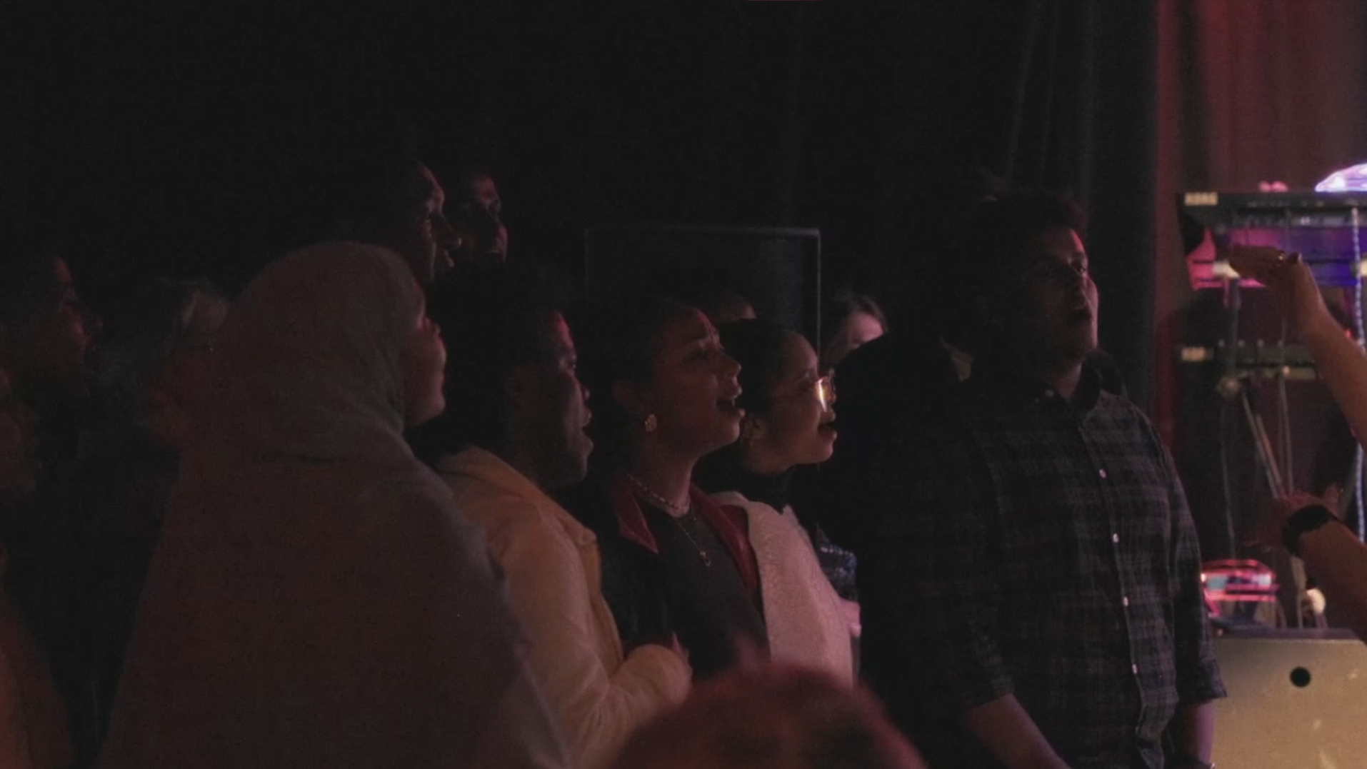 People watching a performance in a dark theater, illuminated by stage lights.