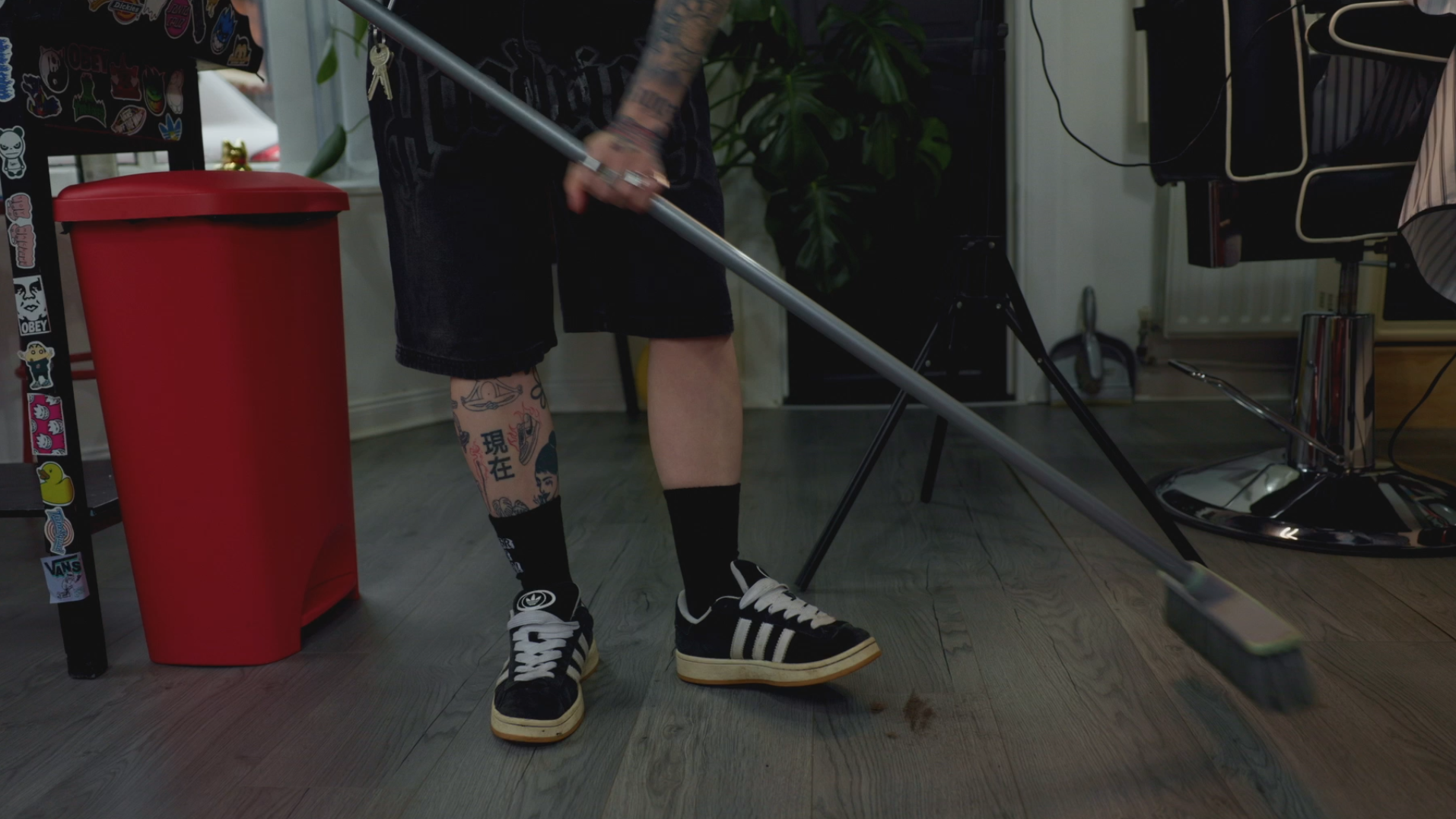 Person cleaning the floor with a mop in a room with tattoos on their legs, wearing black socks and sneakers
