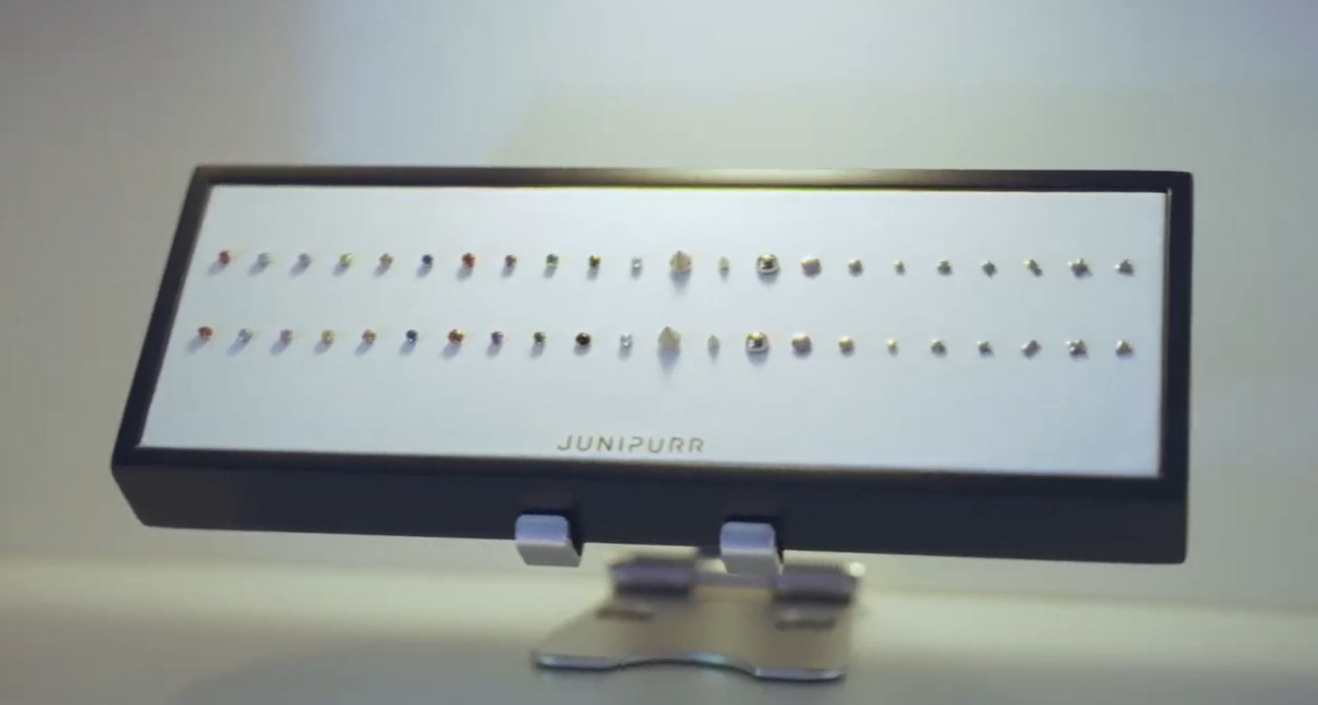 A display case with small, colorful objects, labeled 'JUNIPURR' on a white background.