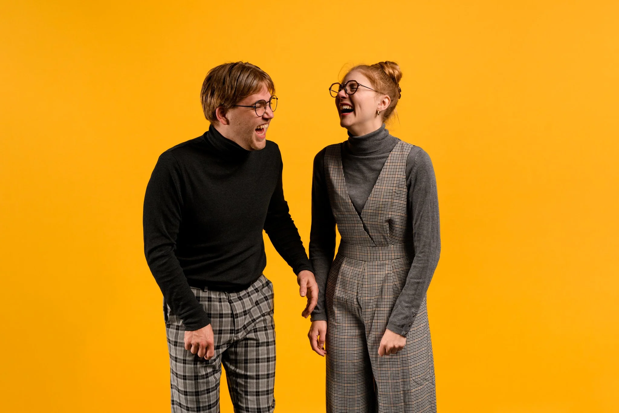 Twee lachende jongeren, een man en een vrouw, die samen lachen tegen een gele achtergrond.