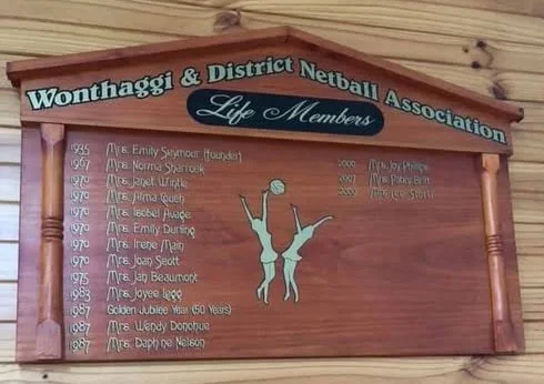 A wooden plaque listing life members of the Wonthaggi & District Netball Association, featuring names and years of membership, with a graphic of two netball players reaching for the ball.