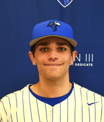 Young man in a blue baseball cap with a black and yellow logo, wearing a white and blue pinstriped jersey, standing in front of a blue background with text.