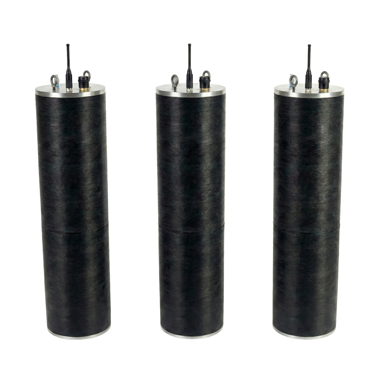 Three large black cylindrical objects with metal tops and connected wires, likely industrial sensors or equipment, mounted on a white surface.