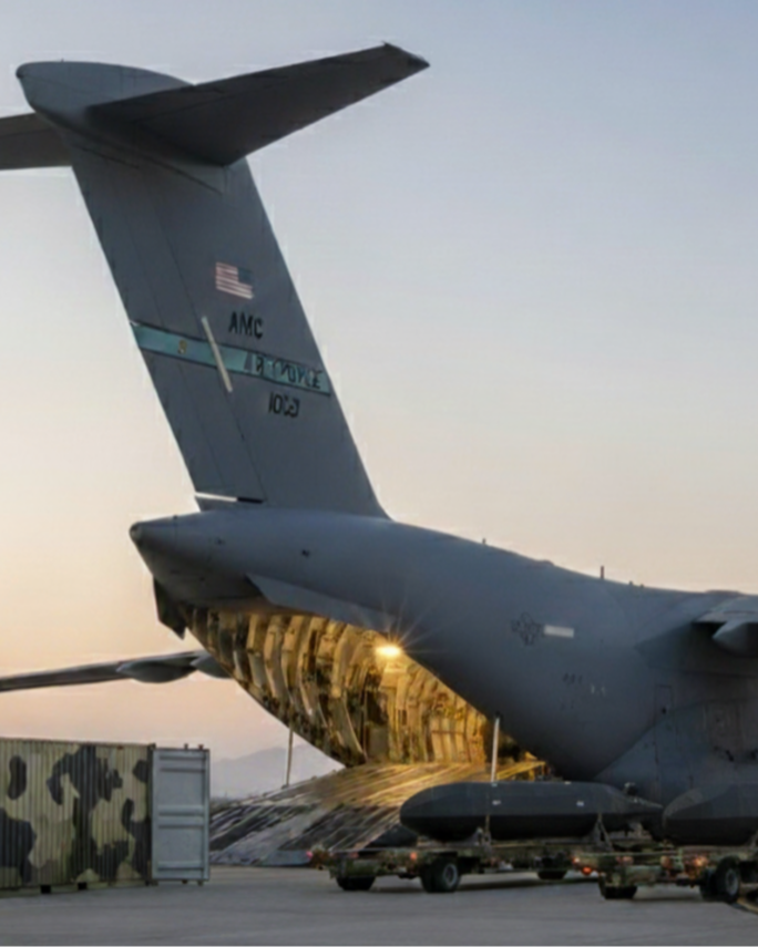 A military cargo aircraft on an airport tarmac with its rear cargo ramp open, revealing the interior. The tail number and markings indicate it is a U.S. Air Force plane.