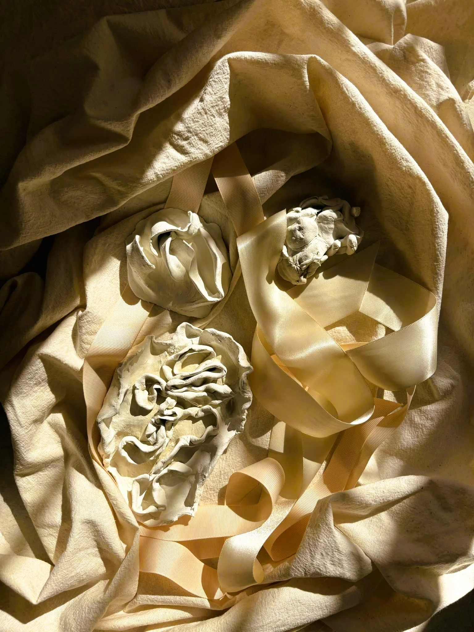 Decorative display with artificial rocks, beige ribbons, and fabric on a soft, textured beige surface.