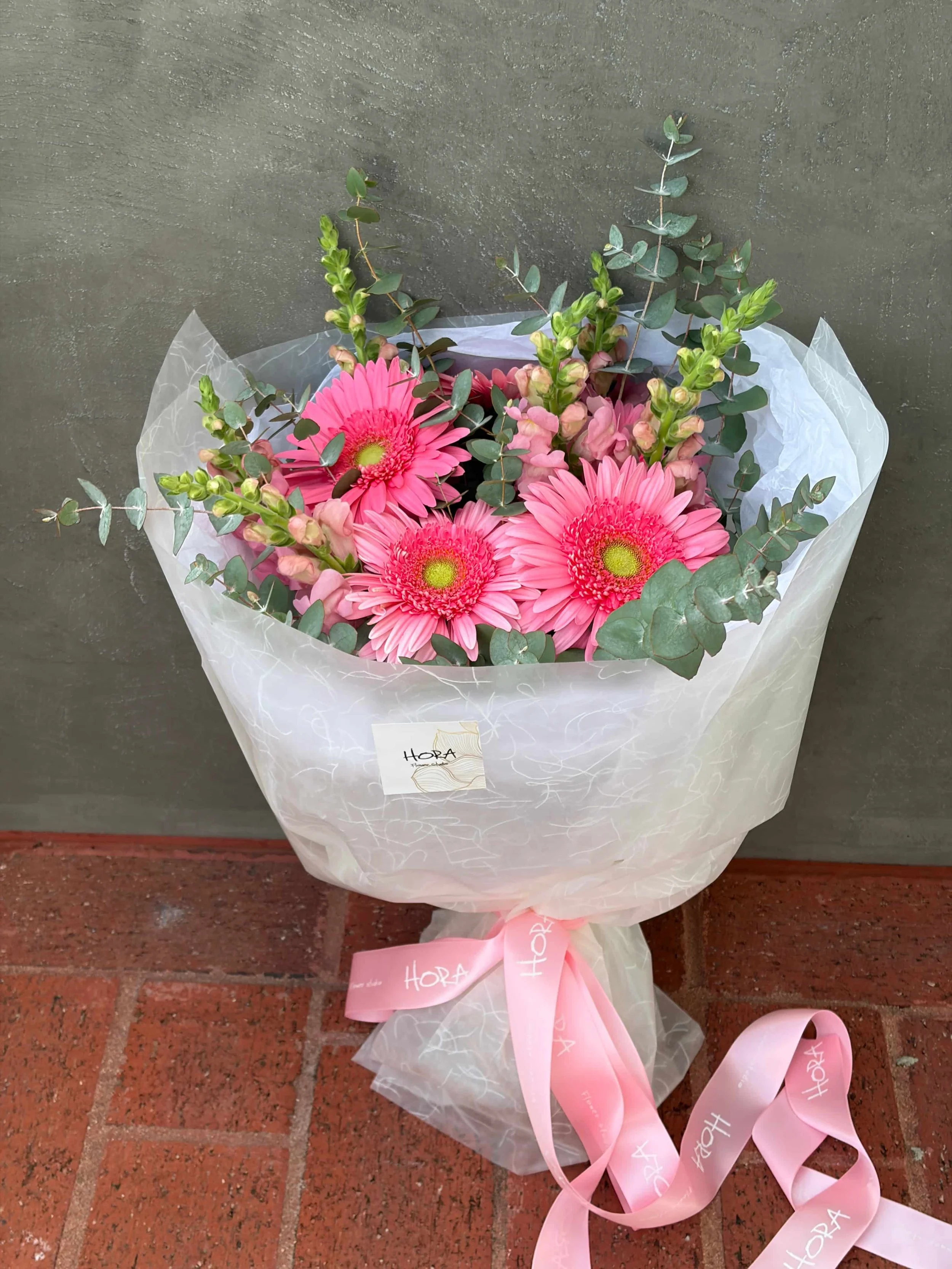 Wrapped pink garden bouquet with gerberas, eucalyptus greenery, and soft seasonal flowers, finished with HORA Flowers ribbon in Perth.