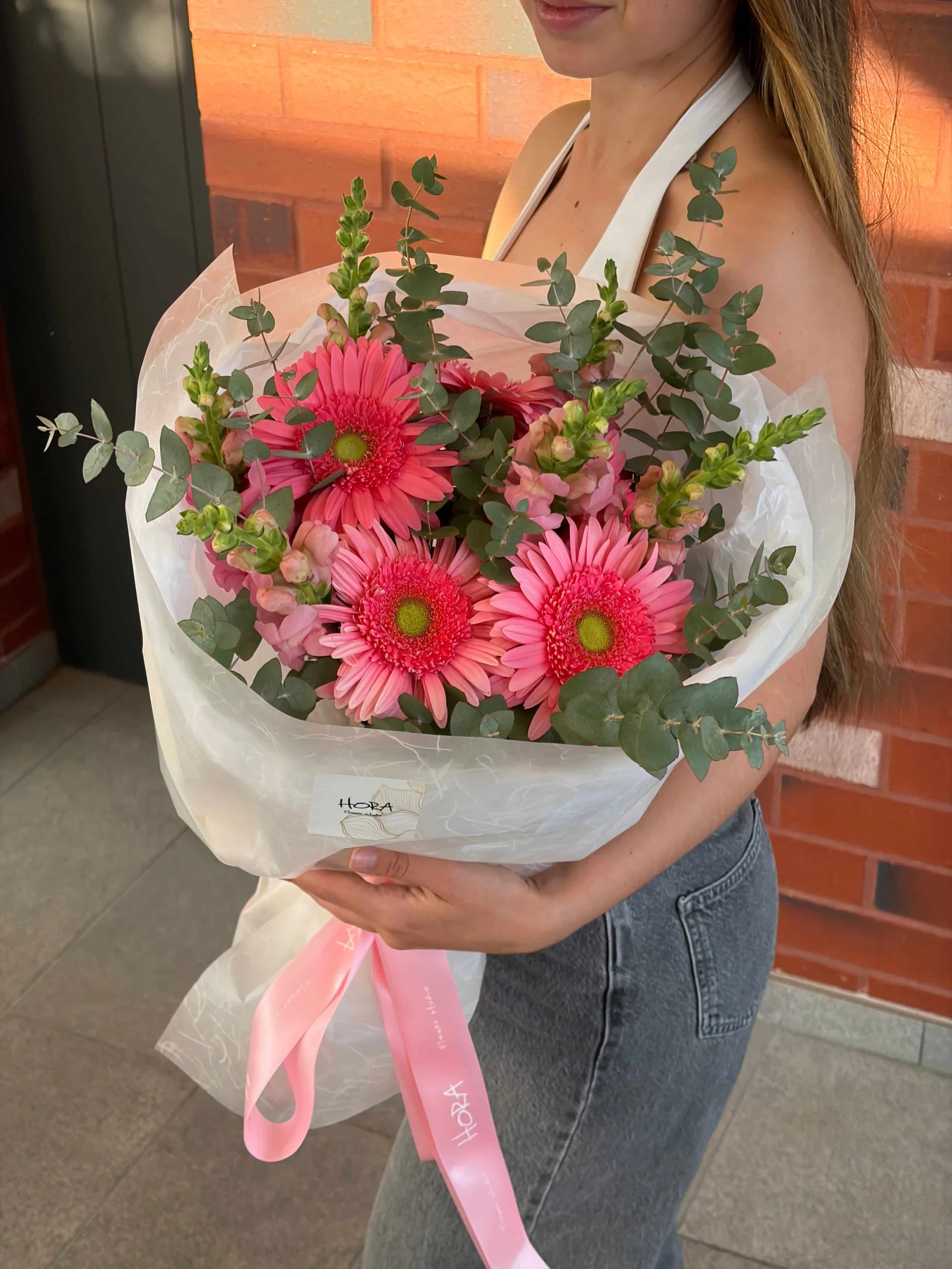 Wrapped pink garden bouquet with gerberas, eucalyptus greenery, and soft seasonal flowers held by a person, designed by HORA Flowers Perth.