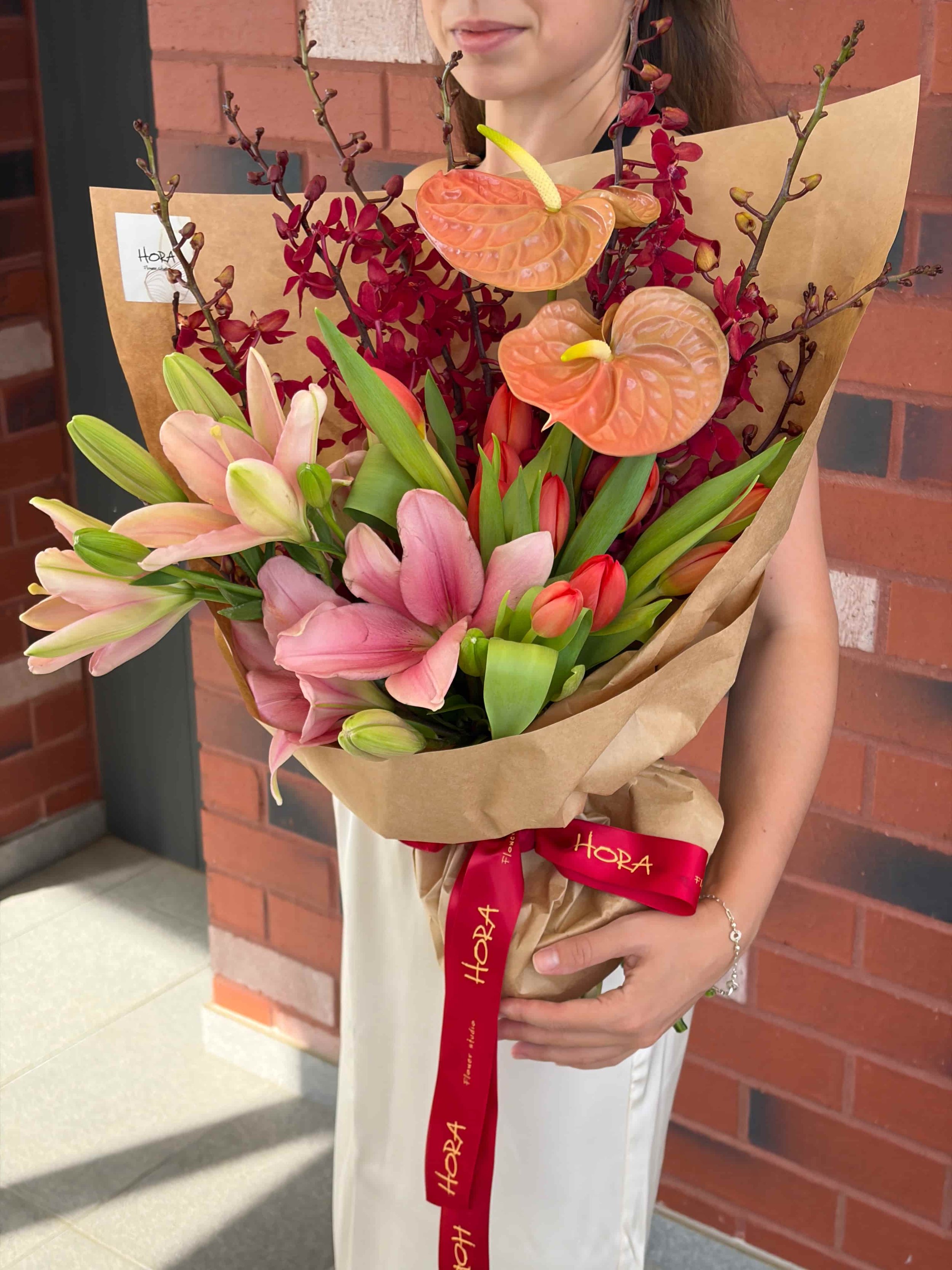 Wrapped pink lily and anthurium bouquet held by hand by HORA Flowers Perth