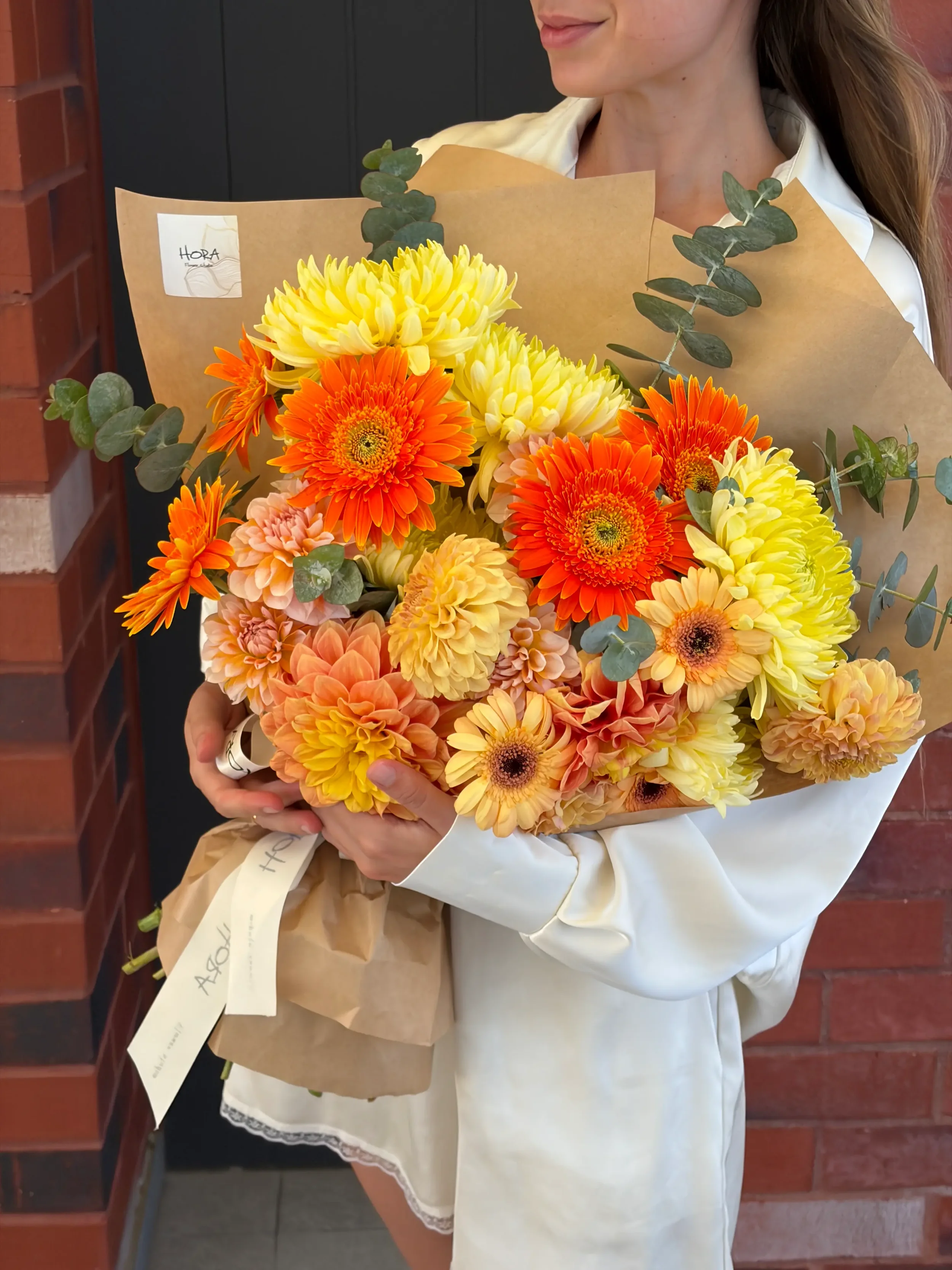 Seasonal bouquet held by model by HORA Flowers Perth in warm orange and yellow tones