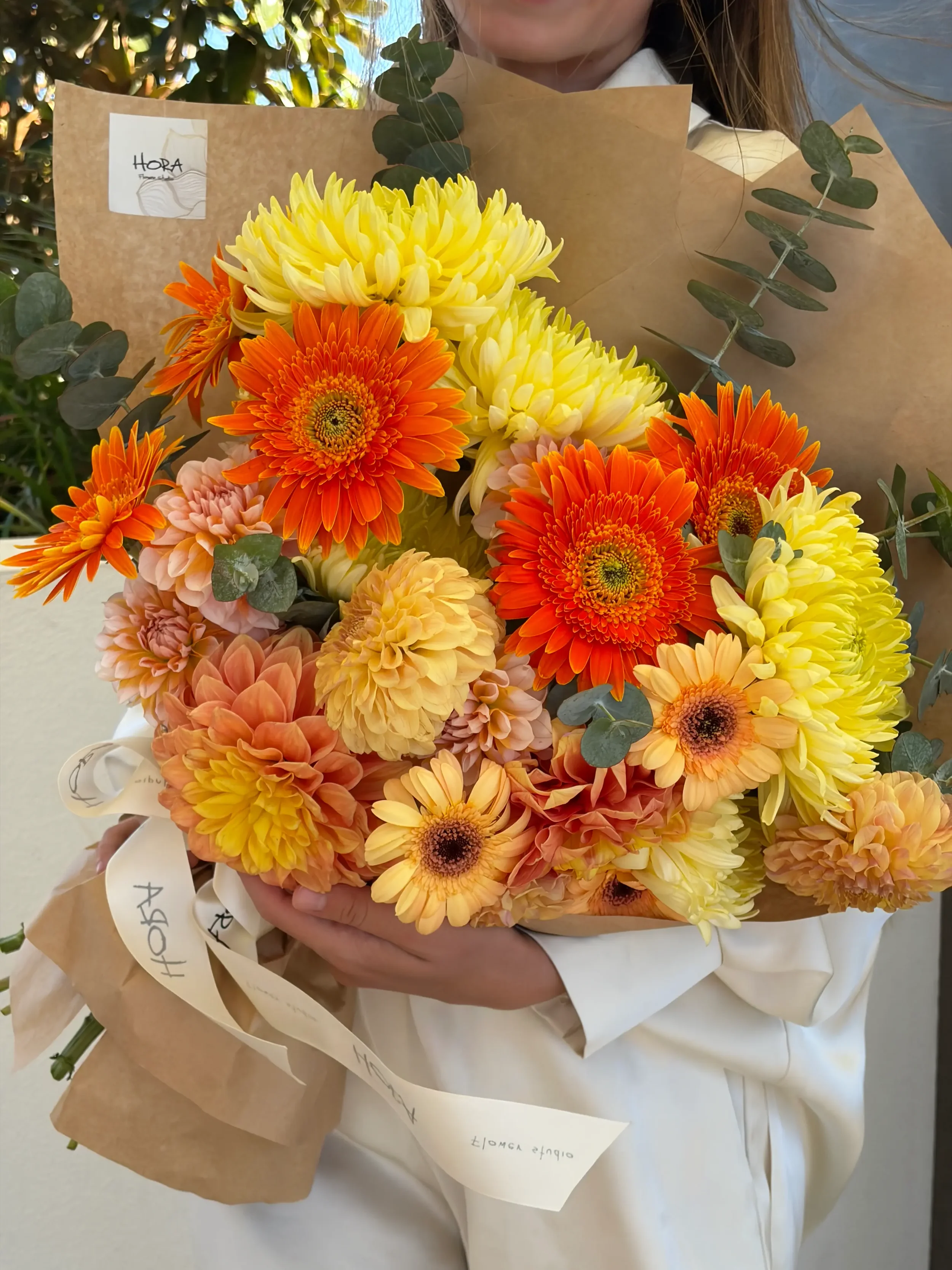 Wrapped seasonal bouquet by HORA Flowers Perth in warm orange and yellow tones