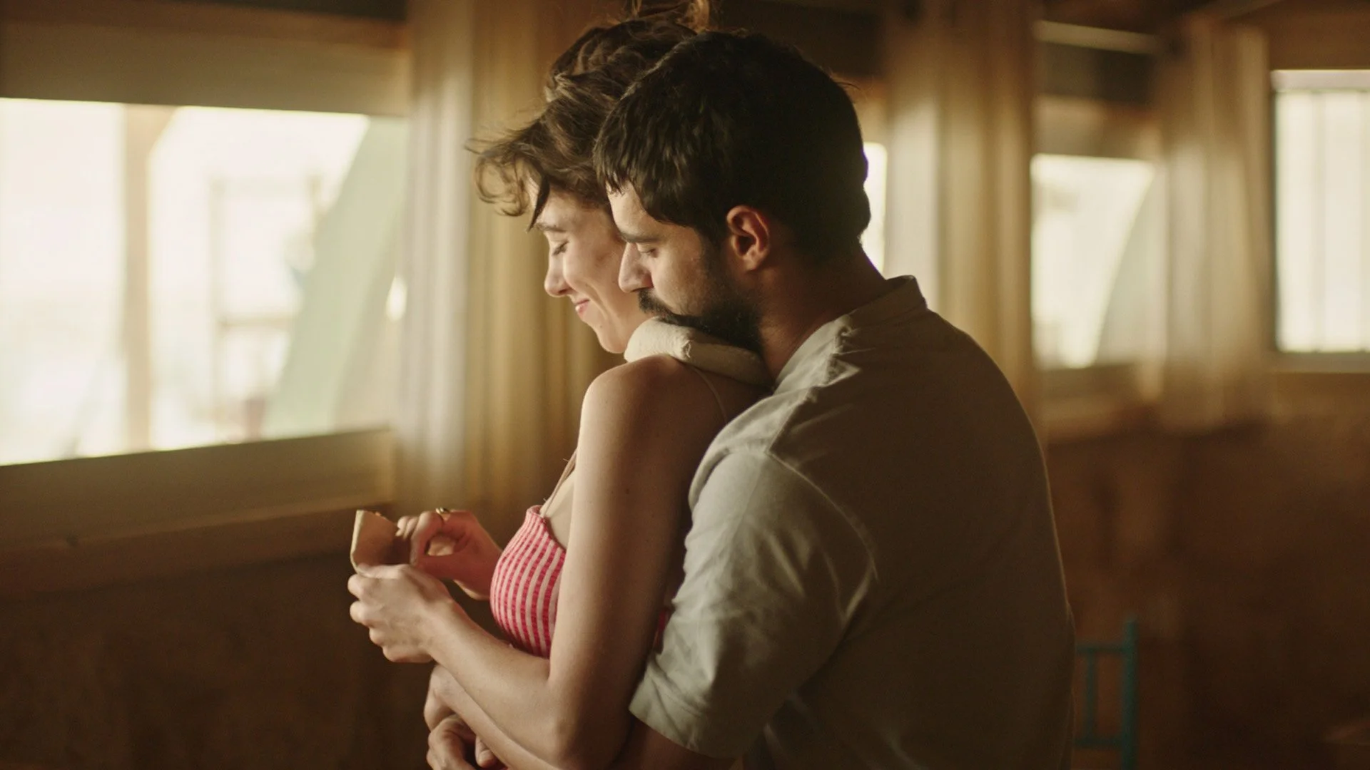 Un couple se câline dans une pièce lumineuse en arrière-plan, avec des fenêtres laissant entrer la lumière naturelle.