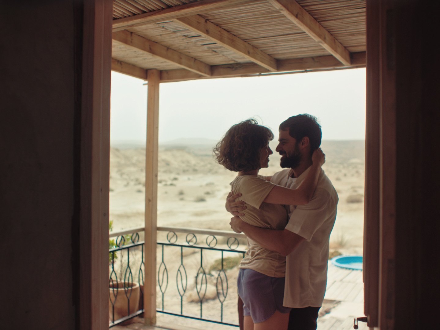 Un couple s'embrasse tendrement sur un balcon regardant le désert, sous un ciel lumineux.
