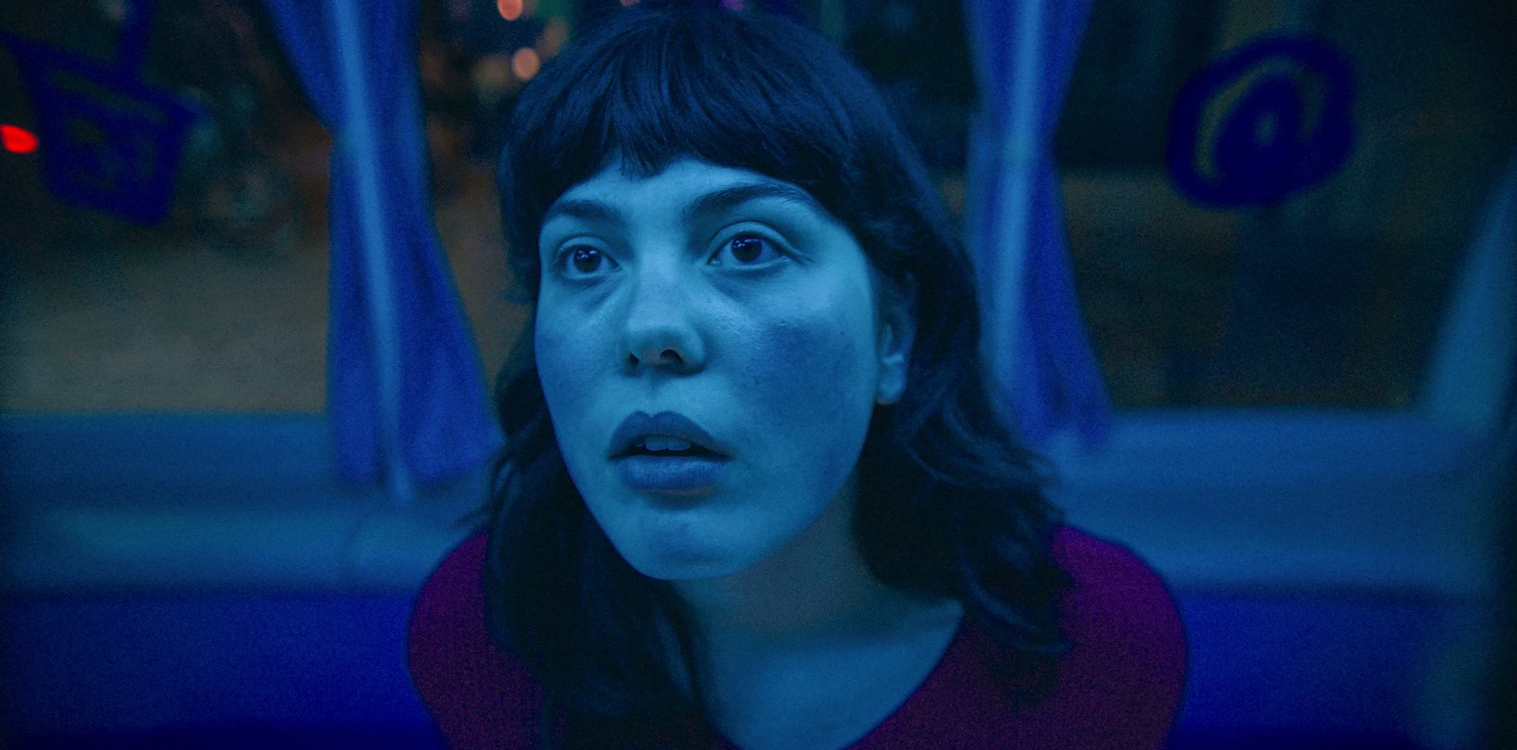 Une femme avec un visage expressif regarde à travers une fenêtre, éclairée par une lumière bleue