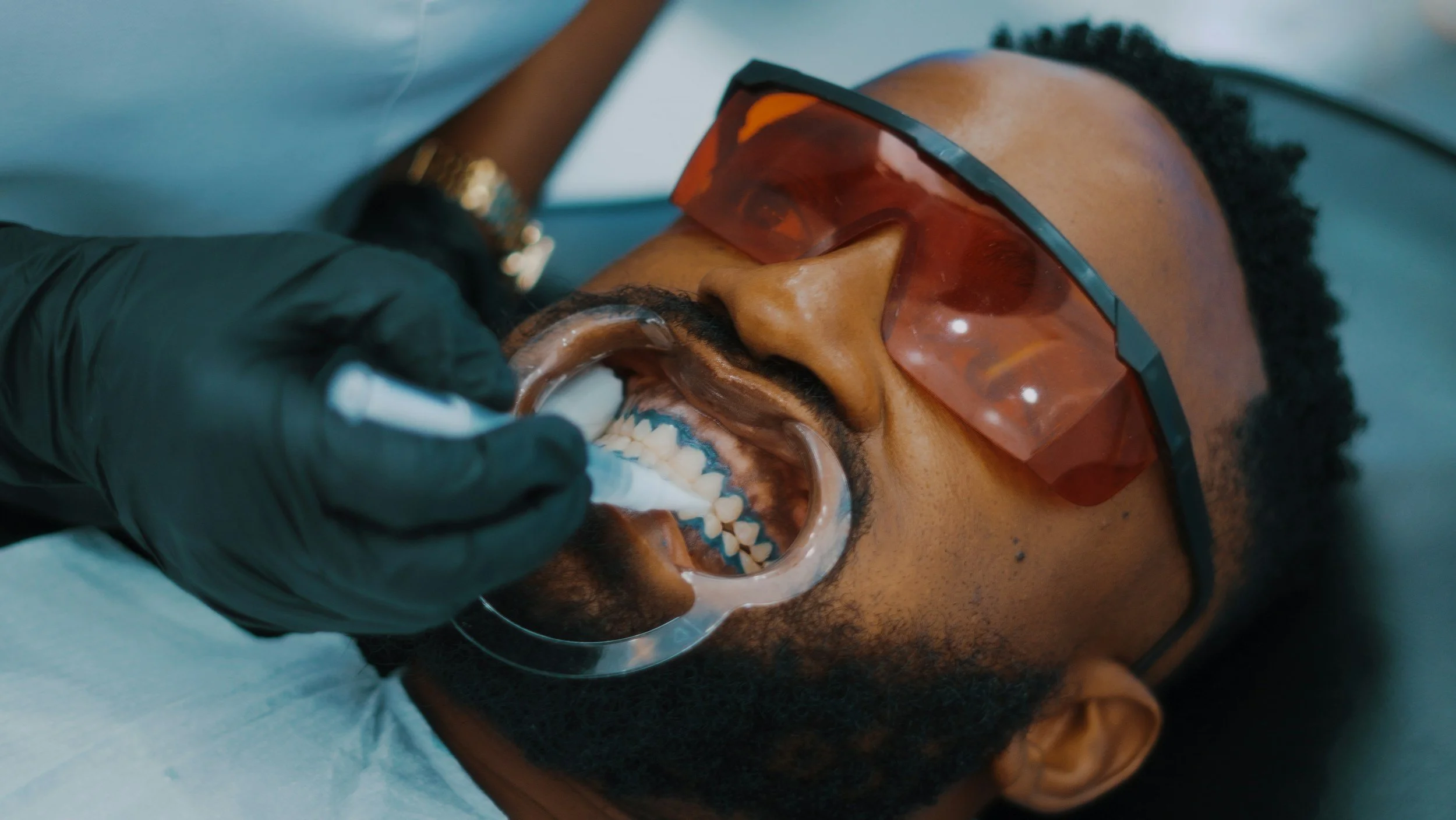 Man wearing protective glasses having dental work done, with dental tool in mouth, at dental clinic.