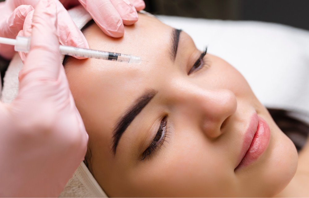 A woman receiving a cosmetic injection in her forehead from a practitioner wearing pink gloves.