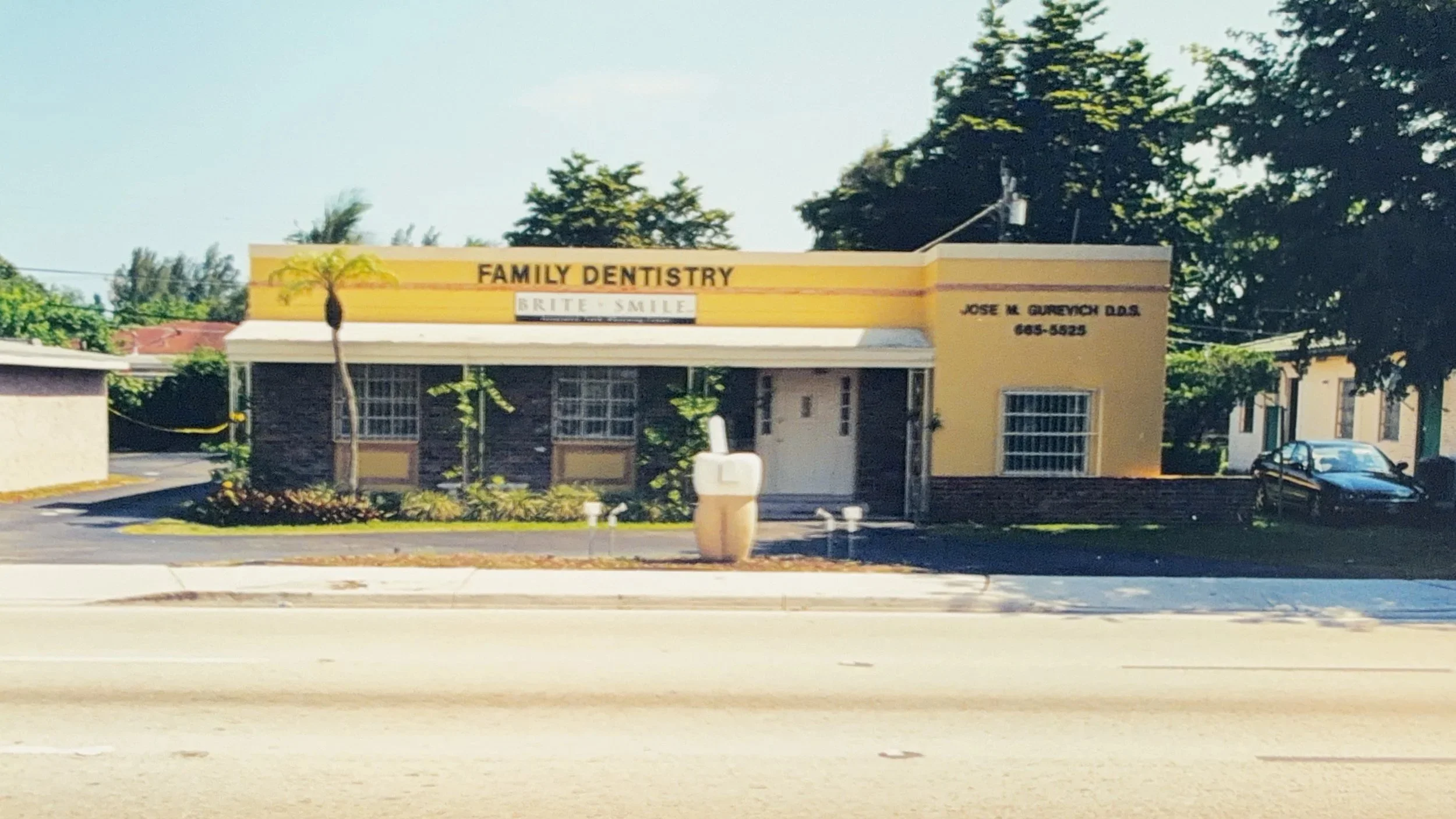 Exterior of a dental office with a yellow facade, palm trees, and cars in the parking lot.