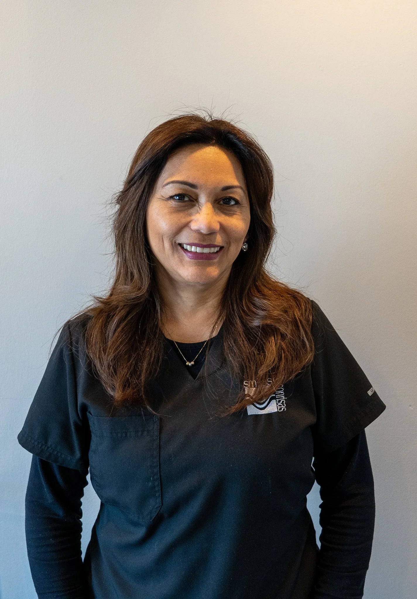 Smiling woman with brown hair wearing a black shirt against a plain light background.