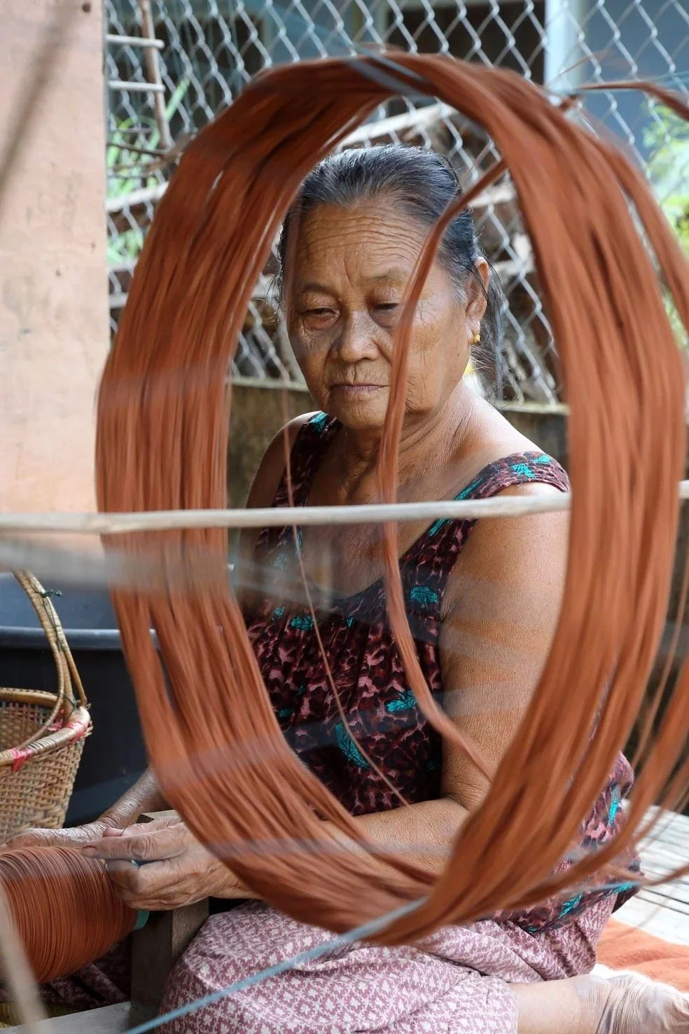 An elderly woman winding a skein of organically dyed brown cotton thread outdoors,
