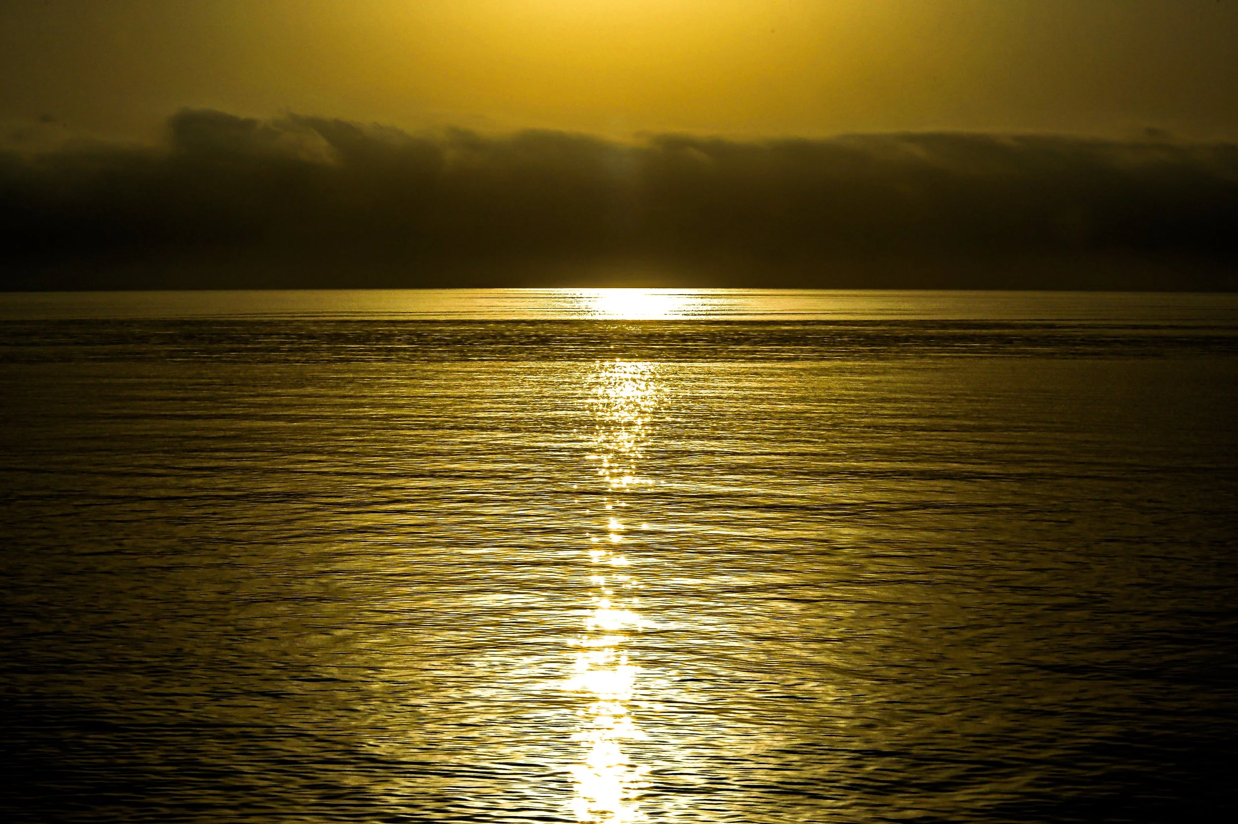 Sunset over a calm ocean with golden reflections on the water and dark clouds in the sky.