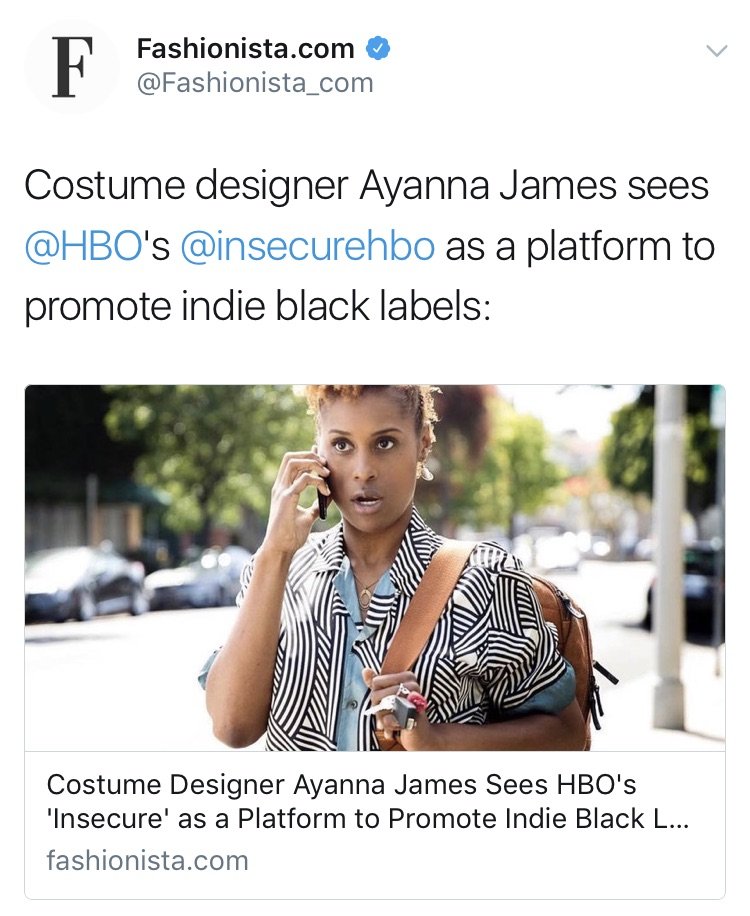 A woman with short curly hair talking on her cellphone while walking outdoors on a city street. She is wearing a black and white patterned shirt and carrying a brown shoulder bag. Background includes trees, cars, and a sidewalk.