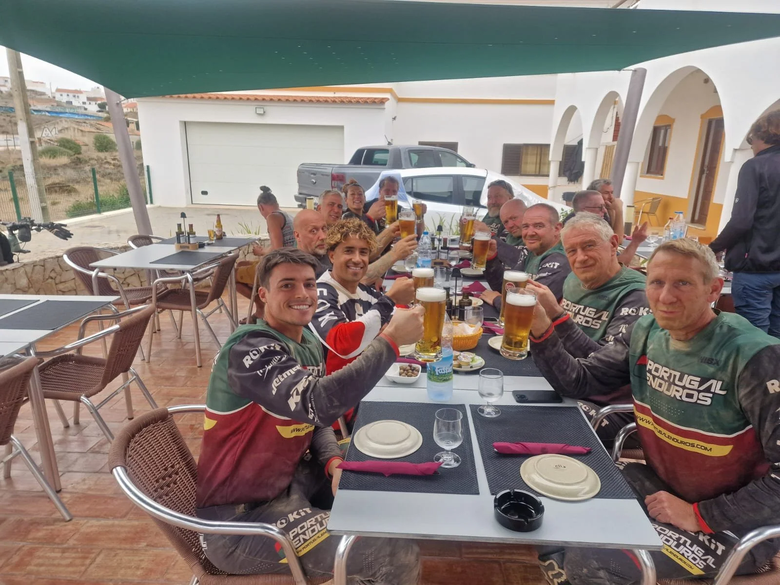 A group of friends at an outdoor restaurant, raising glasses of beer in a toast, smiling and enjoying a gathering.