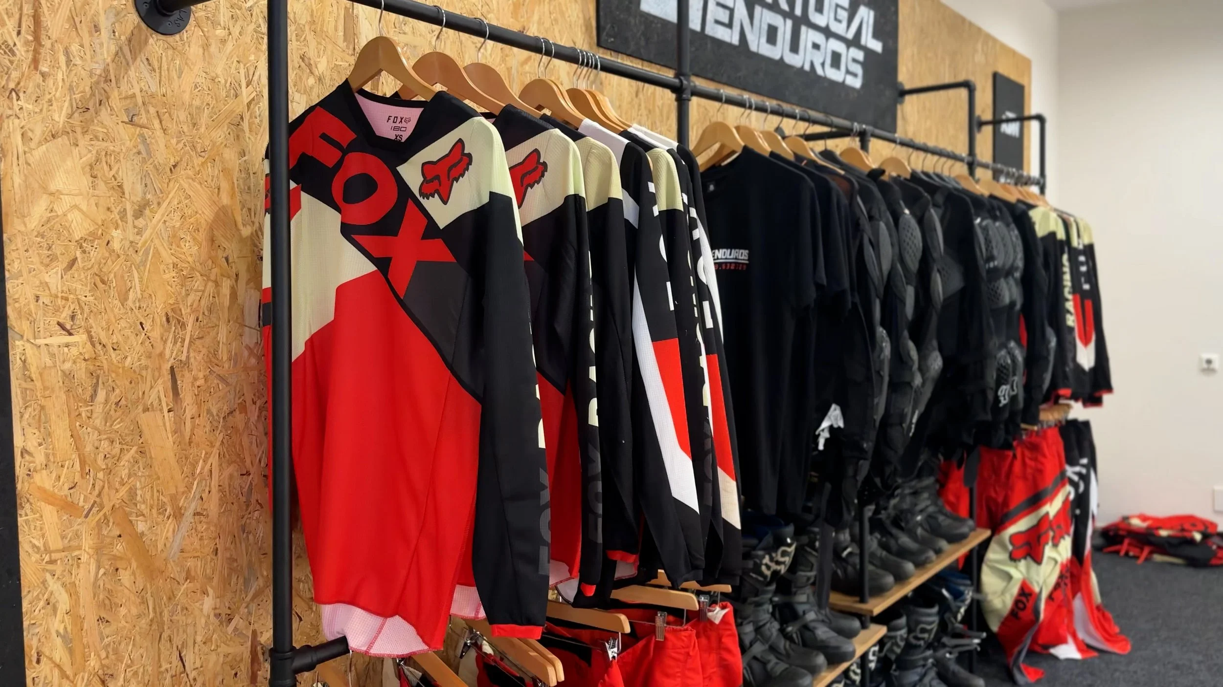 Racing gear including jerseys, jackets, gloves, and boots neatly arranged on racks at a sports shop or showroom.
