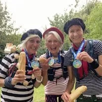 Three women wearing striped shirts and Santa hats, holding ice cream cones, with trees in the background.